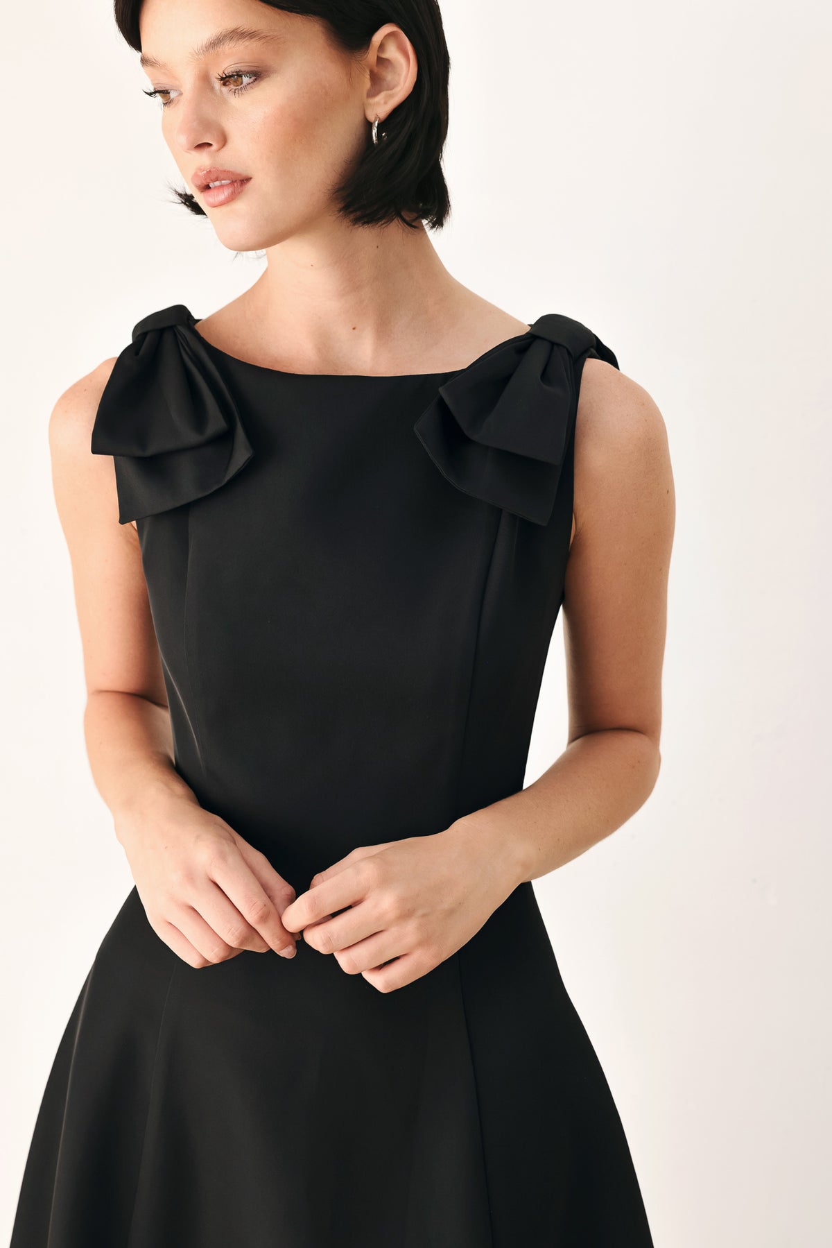A woman modeling a sleeveless black midi dress with a boat neckline and large bow details on the shoulders | FREEMARKET