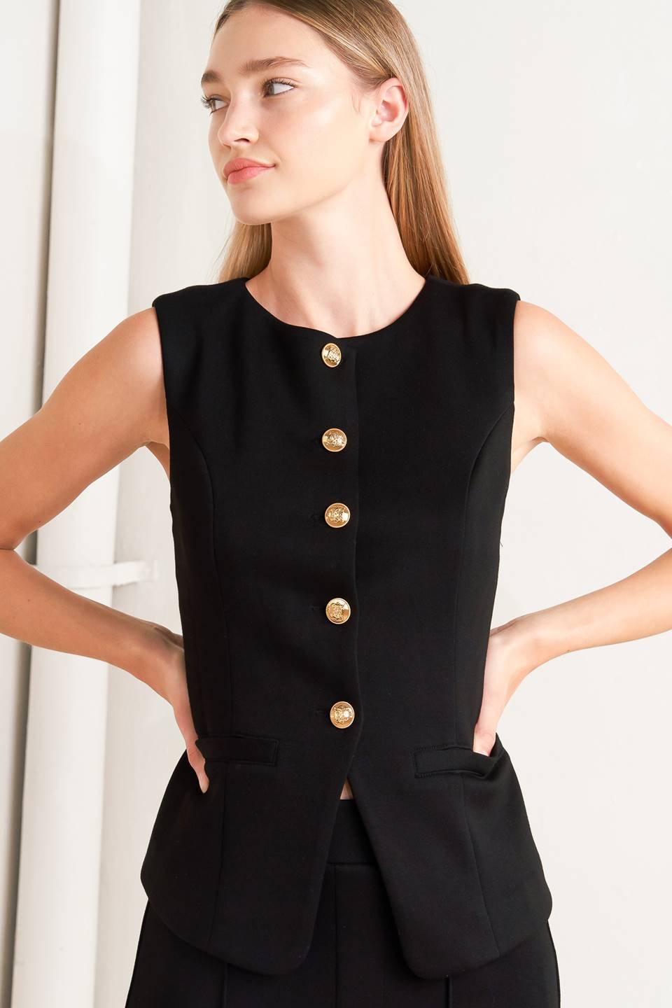 Woman wearing a black sleeveless blazer with gold buttons on a white background - FLYING TOMATO