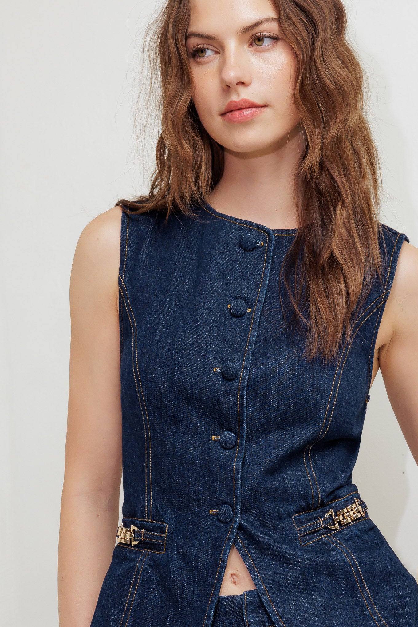 A denim vest featuring round neckline, sleeveless, front button down and hardware trim.