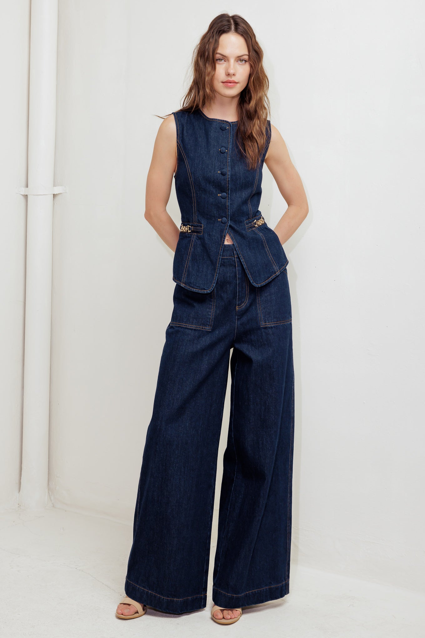 A denim vest featuring round neckline, sleeveless, front button down and hardware trim.