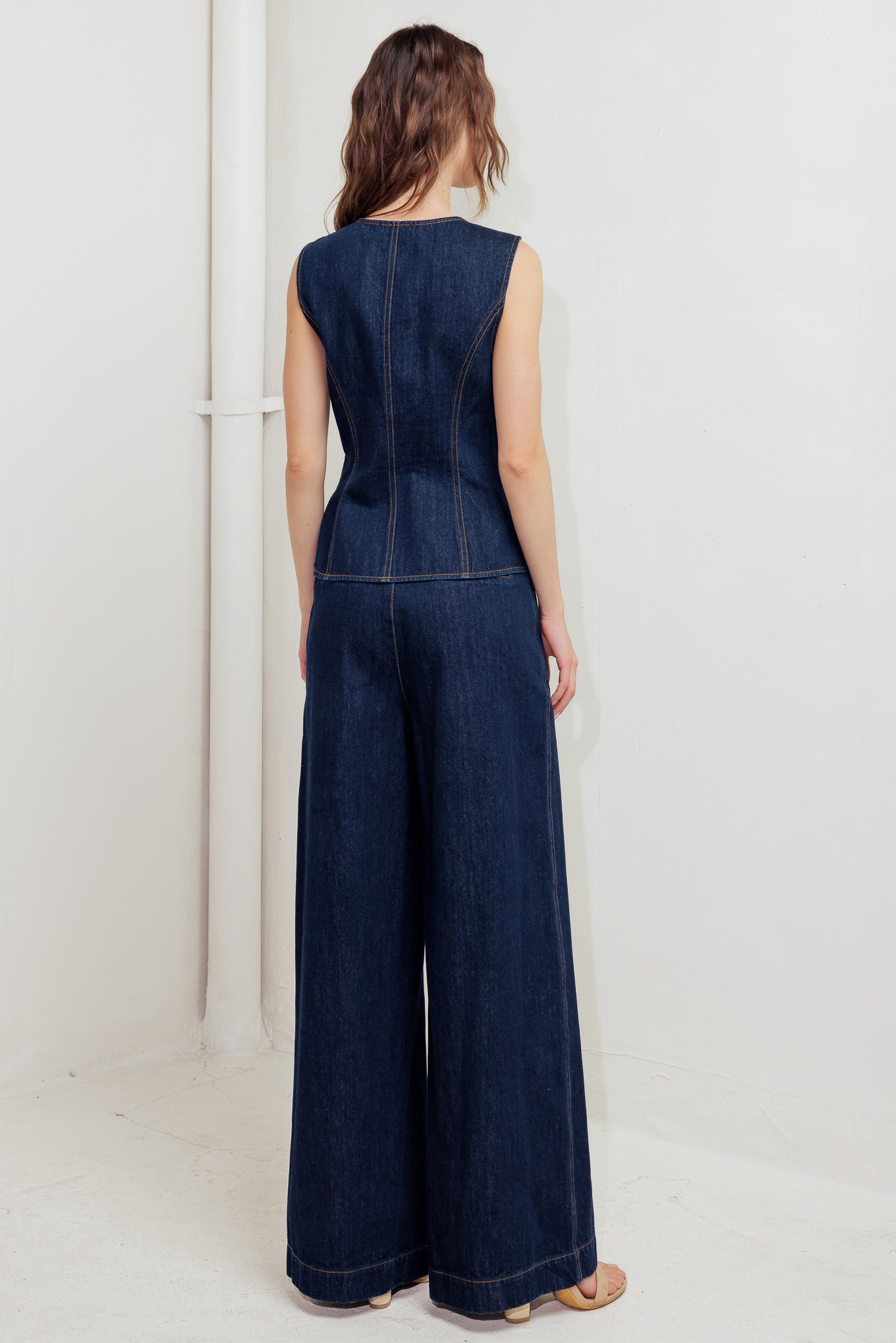 A denim vest featuring round neckline, sleeveless, front button down and hardware trim.