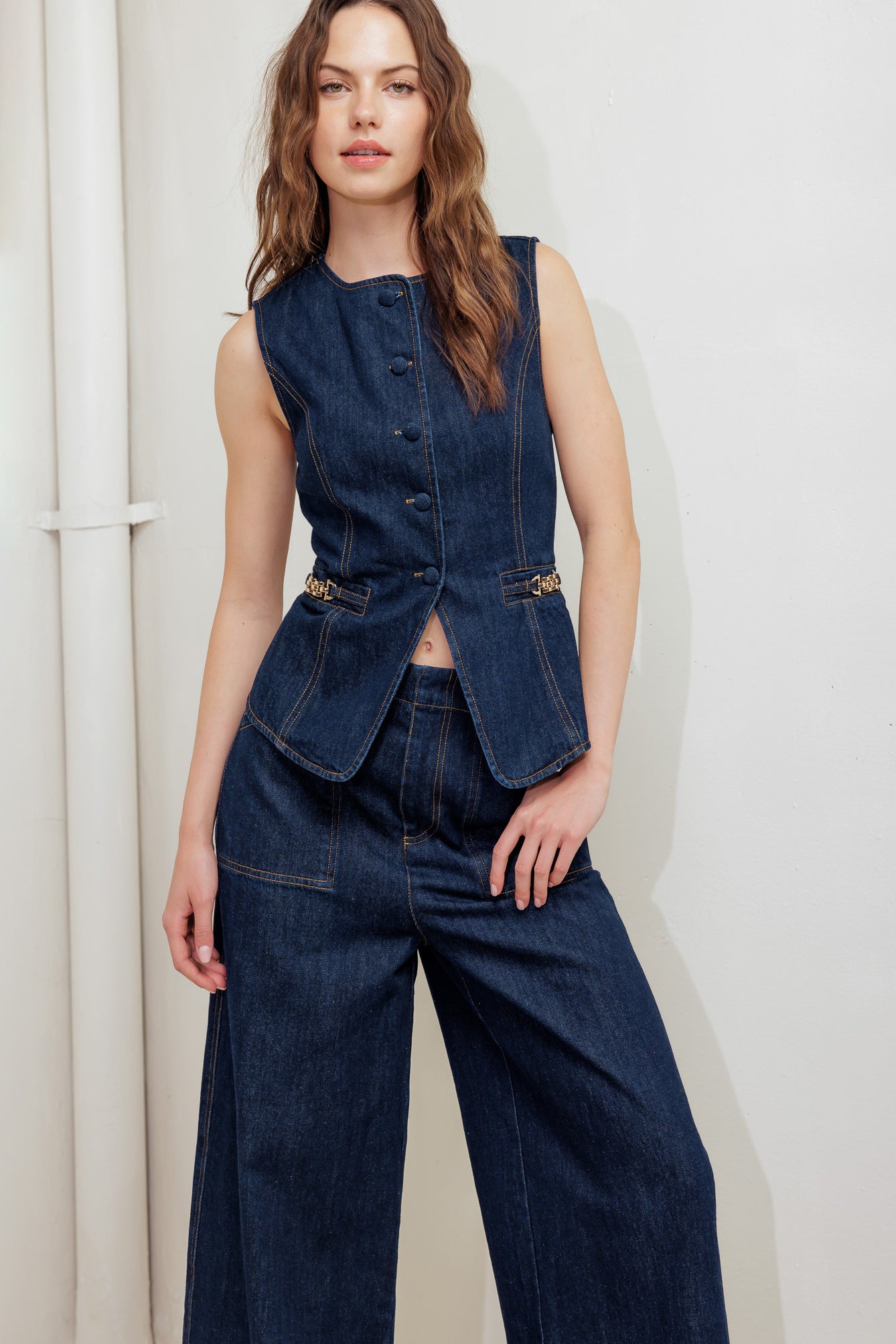 A denim vest featuring round neckline, sleeveless, front button down and hardware trim.