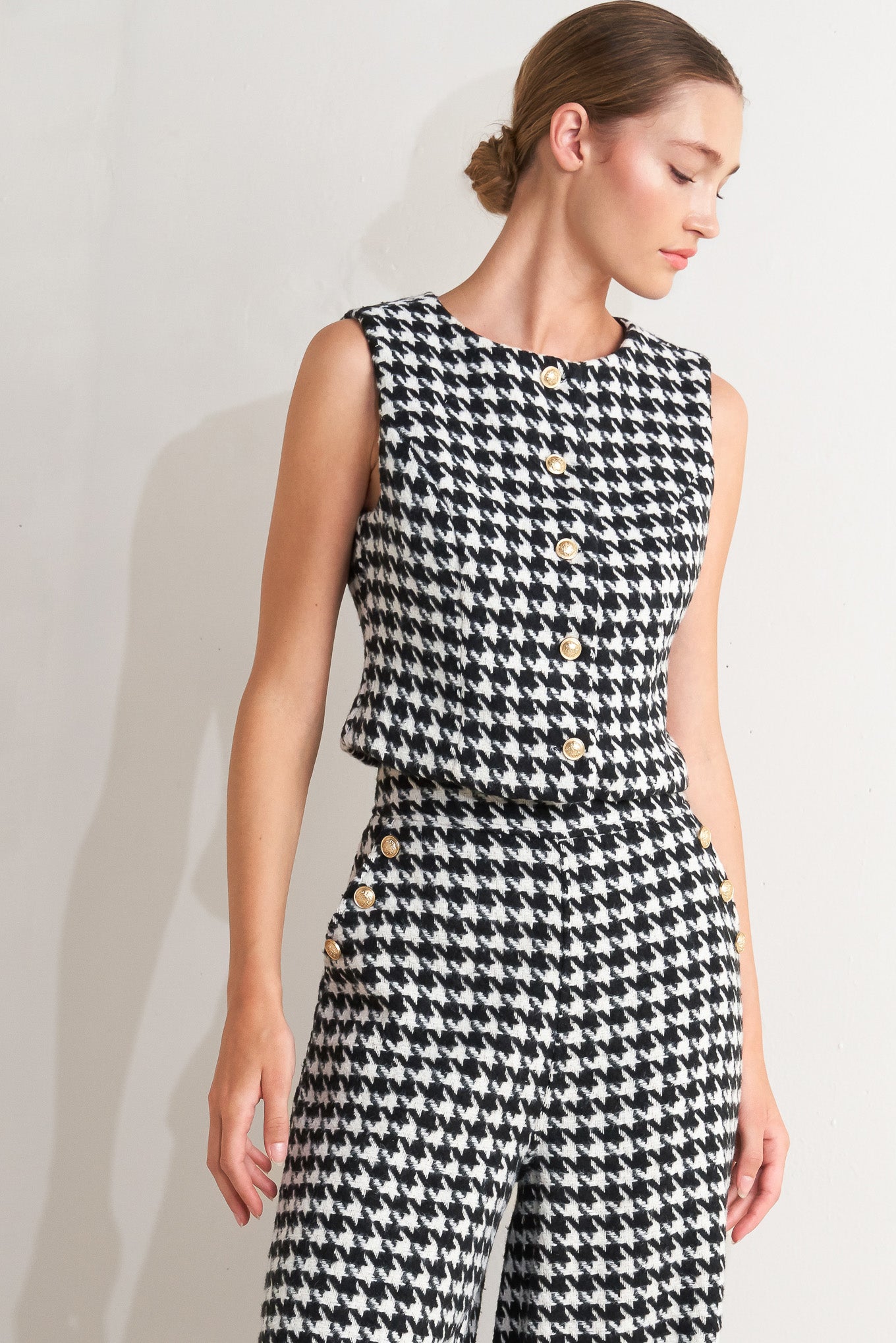 A woven houndstooth vest featuring round neckline, sleeveless and front button down.