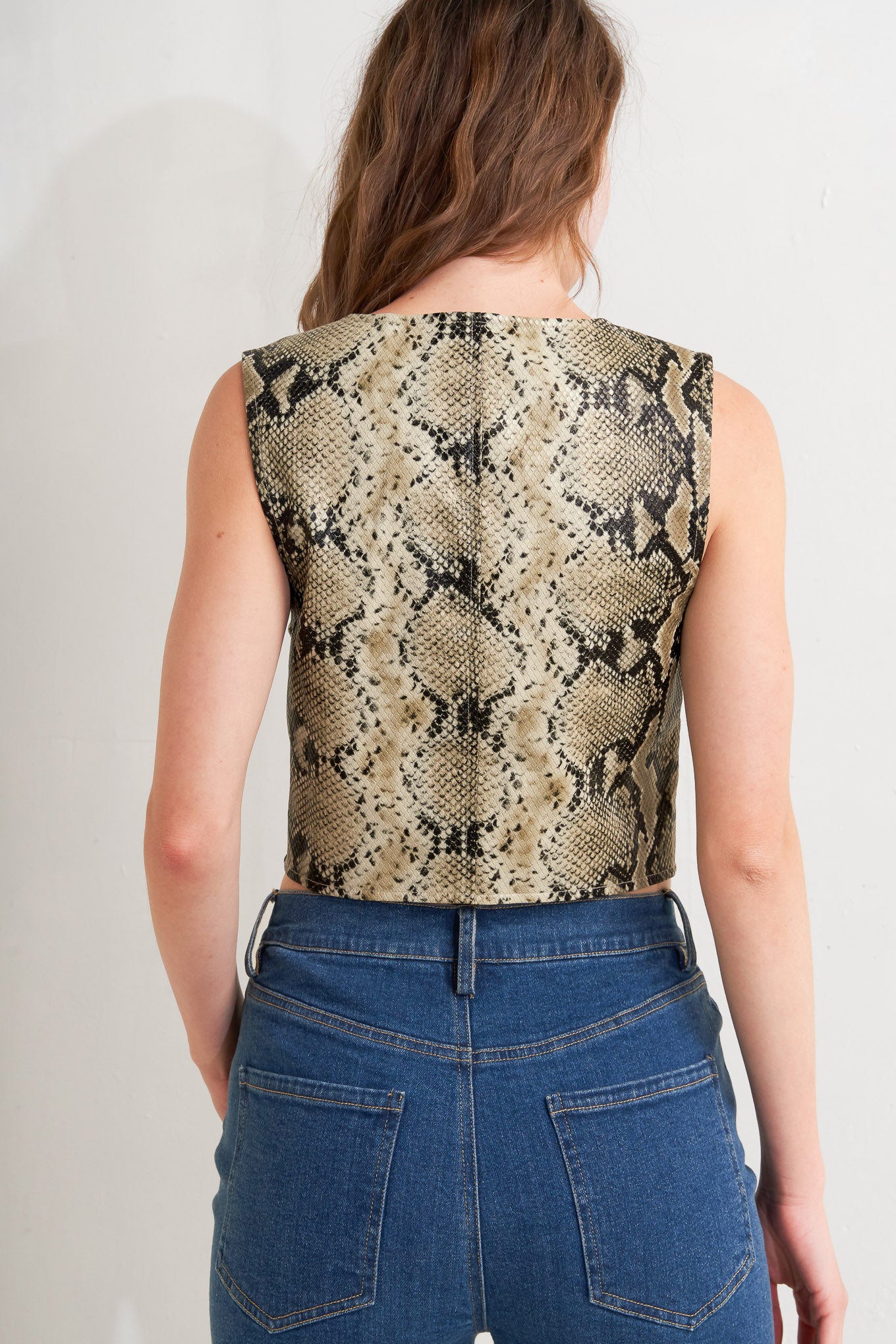 A snake-printed cropped faux leather vest with front button closure.