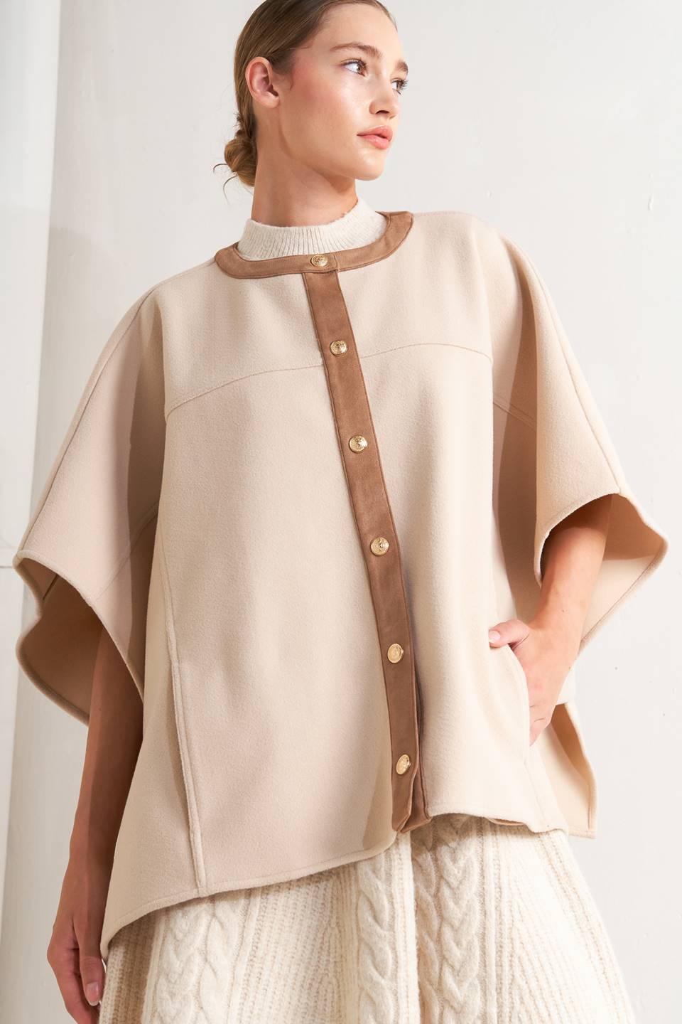 A woven felt capelet featuring round neckline with faux leather binding, front button down and side tab