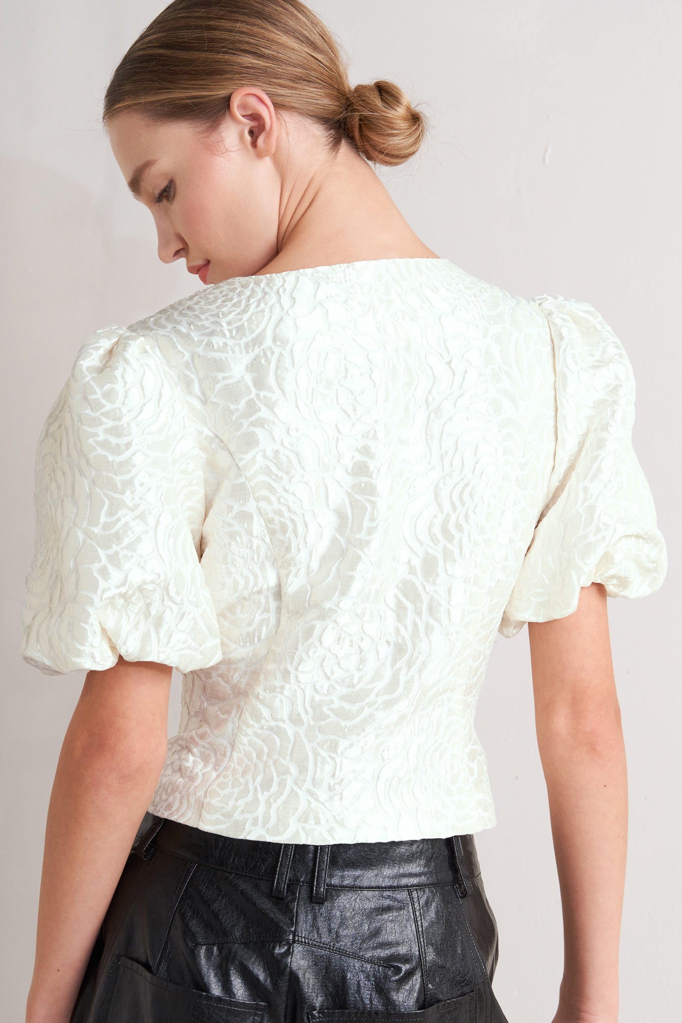 A textured woven top featuring round neckline, short puff sleeve and front button down.