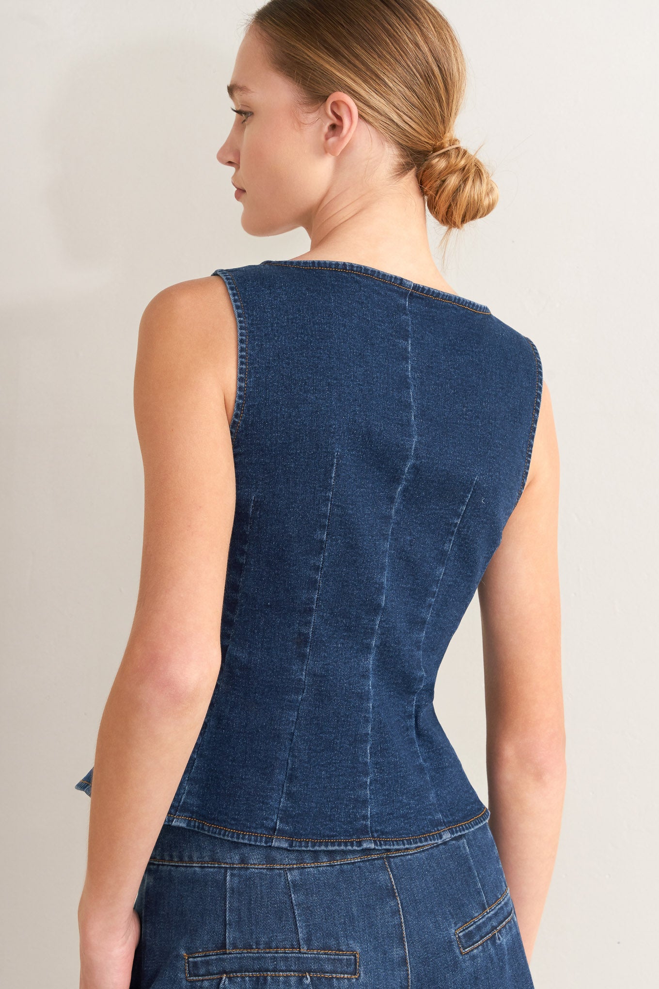 Woman wearing a blue denim top and jeans on a plain background