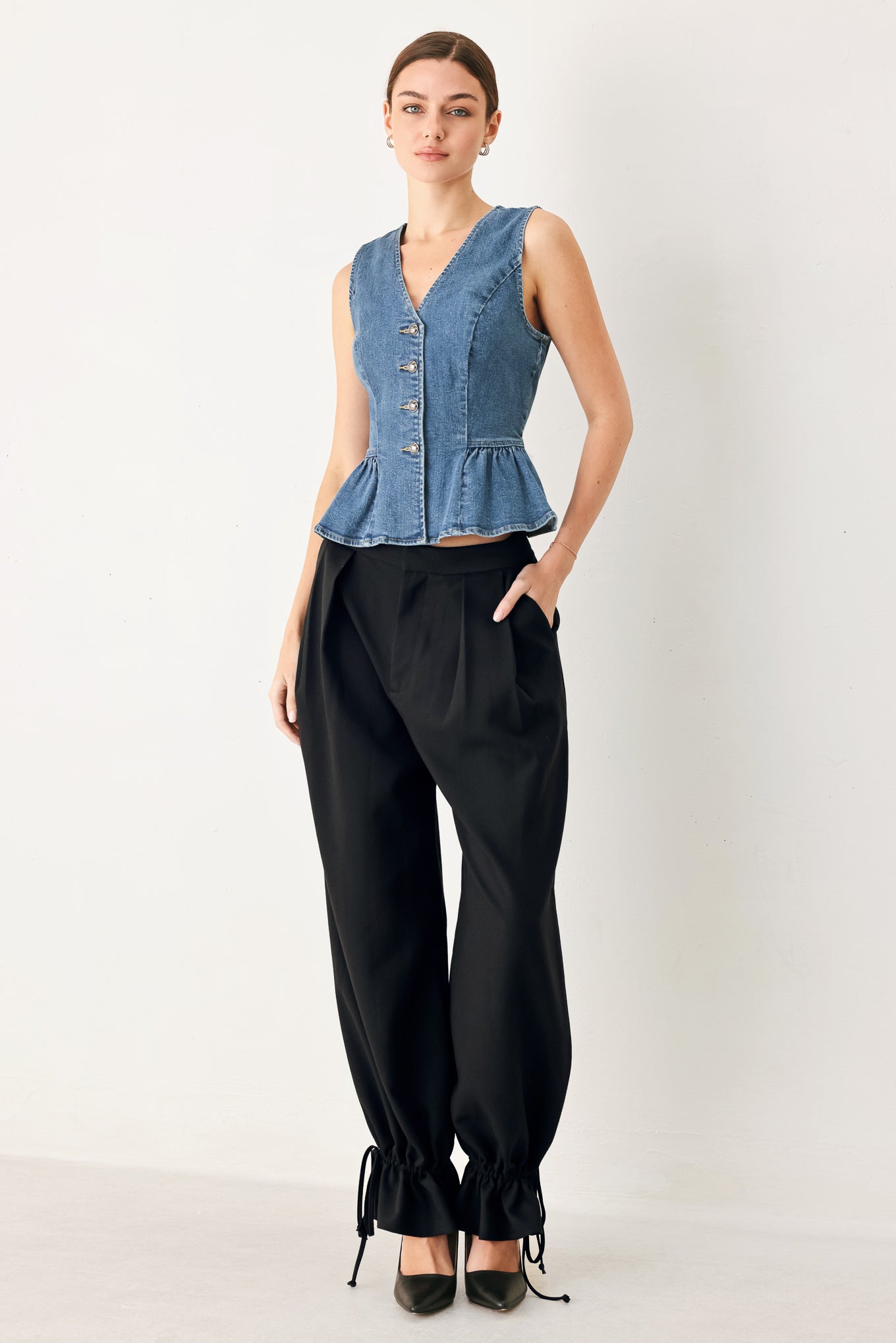 Woman wearing a sleeveless denim peplum vest with V neckline, front button down and side shirring detail | FREEMARKET