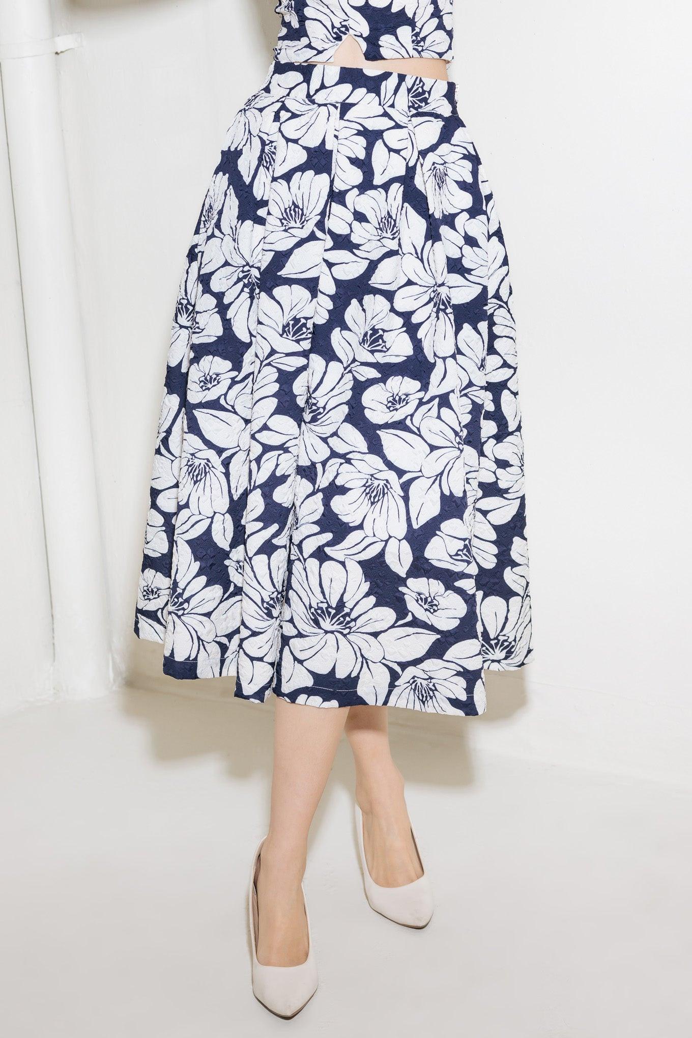 A navy woven midi skirt with a floral print, featuring inverted pleats, a side pocket, and a side zipper closure. Flying Tomato