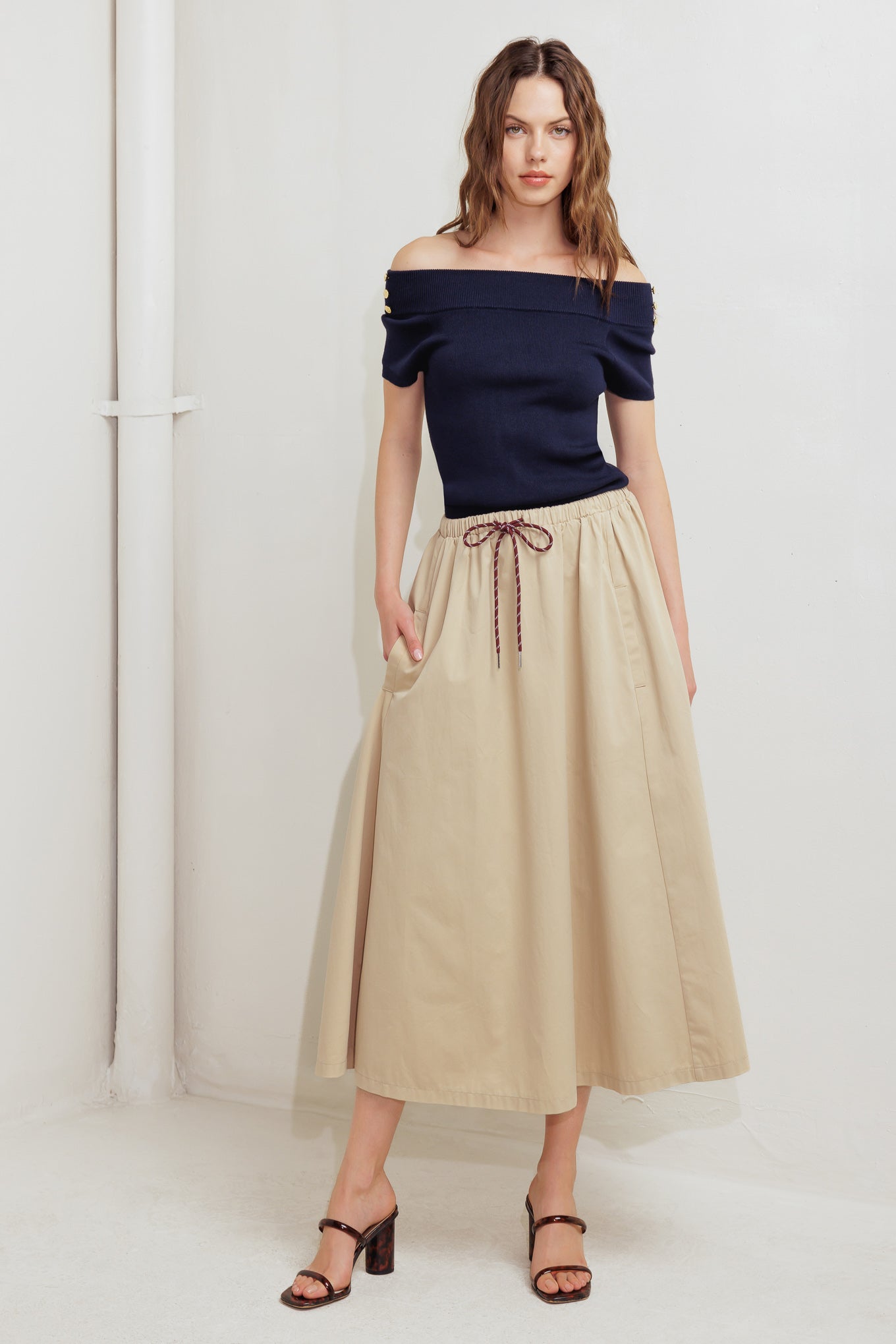 A solid woven midi skirt featuring elasticized waistband with contrasting front tie, side pockets and full skirt
