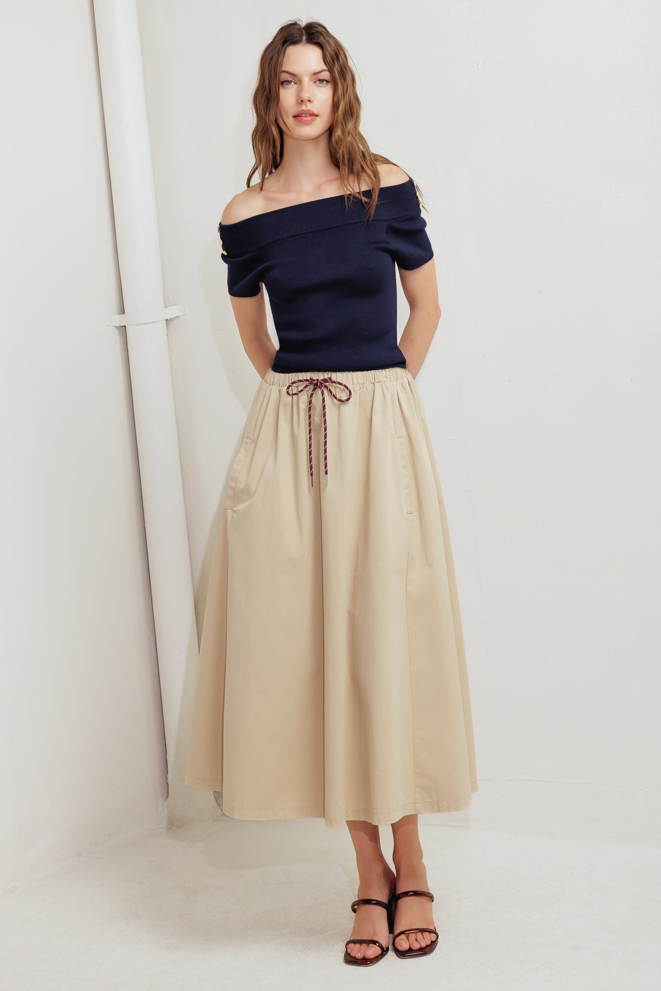 A solid woven midi skirt featuring elasticized waistband with contrasting front tie, side pockets and full skirt