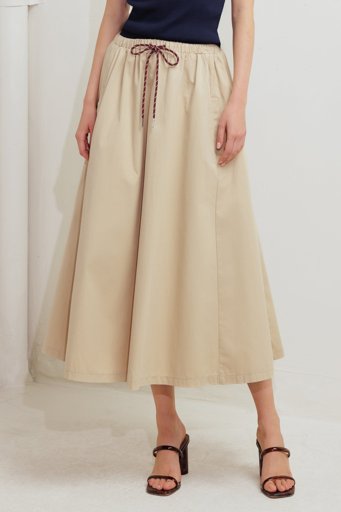 A solid woven midi skirt featuring elasticized waistband with contrasting front tie, side pockets and full skirt