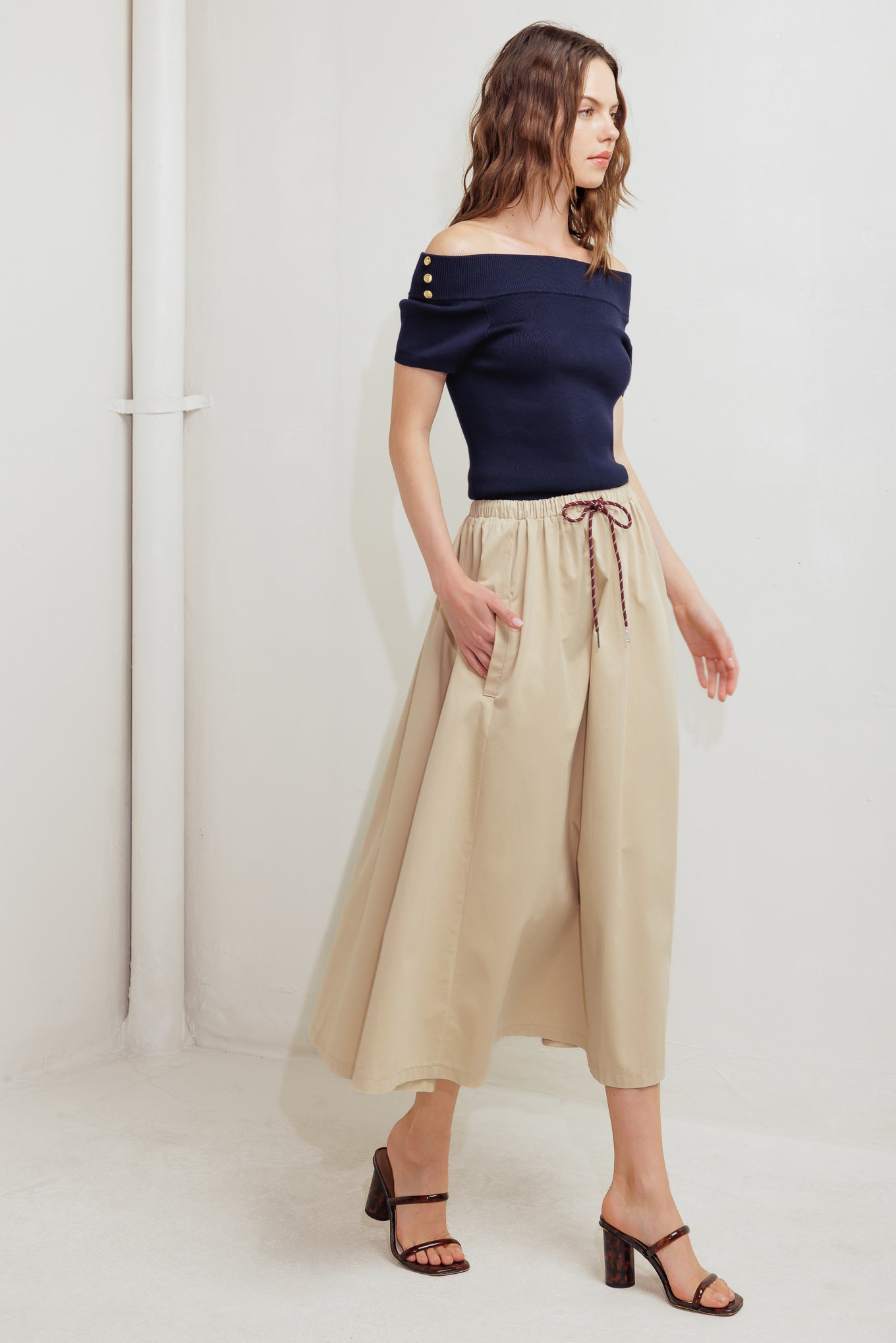 A solid woven midi skirt featuring elasticized waistband with contrasting front tie, side pockets and full skirt