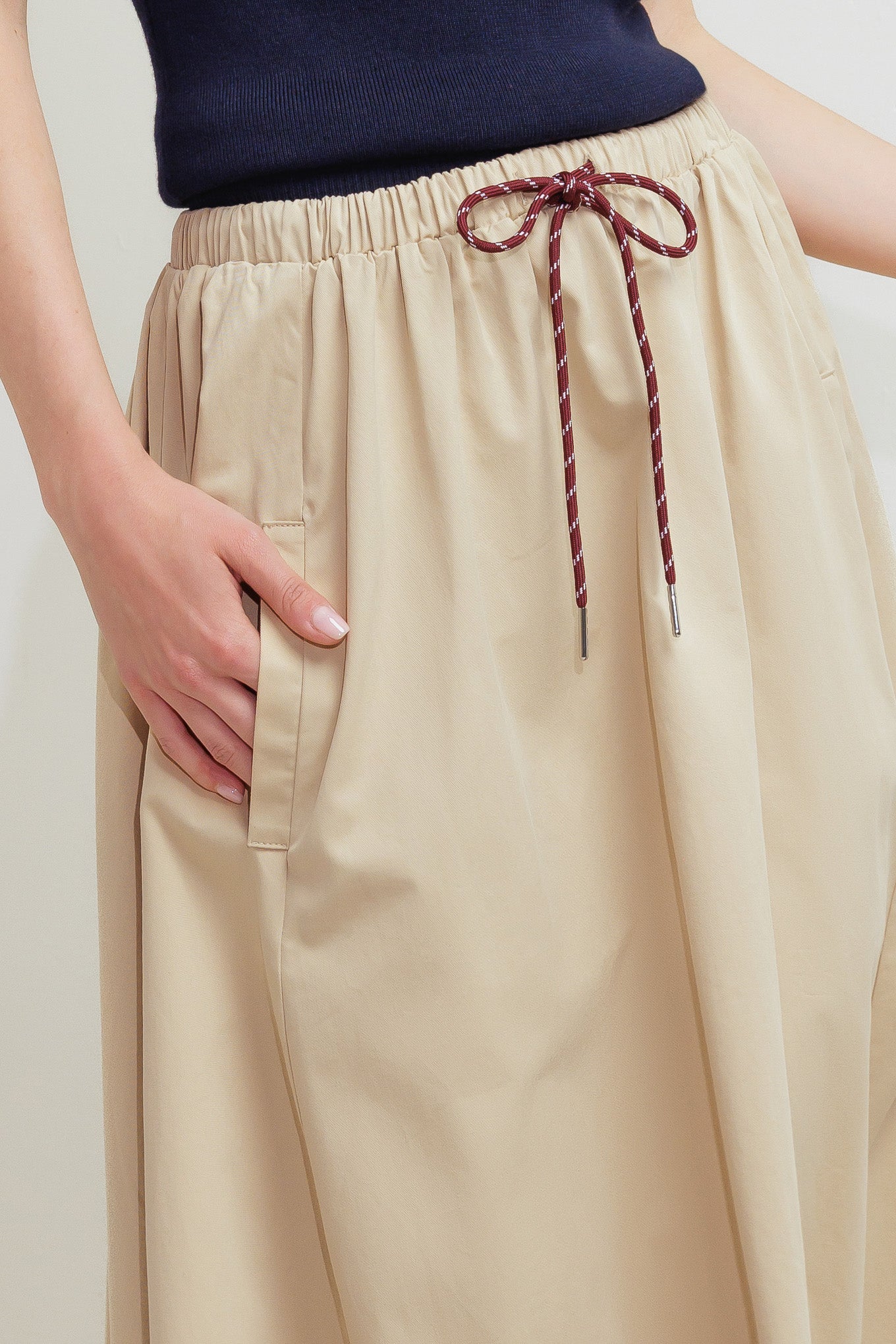 A solid woven midi skirt featuring elasticized waistband with contrasting front tie, side pockets and full skirt