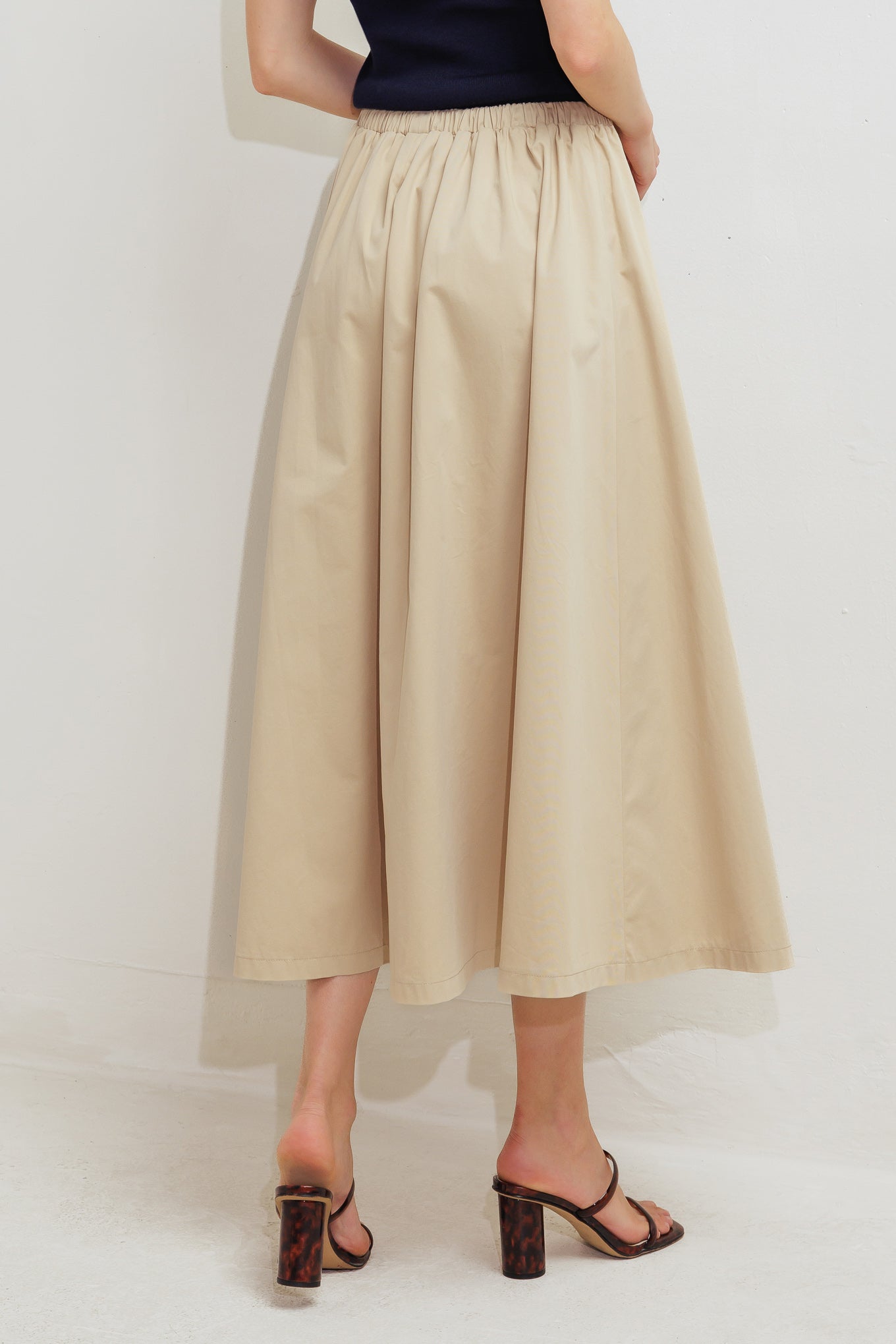 A solid woven midi skirt featuring elasticized waistband with contrasting front tie, side pockets and full skirt