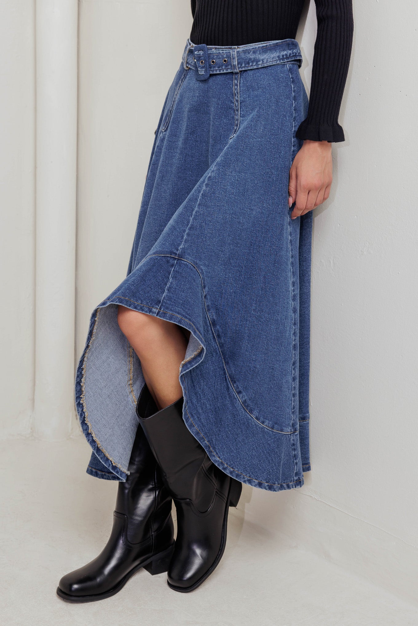 A washed denim midi skirt featuring circle skirt, self belt, uneven hemline and back zipper closure