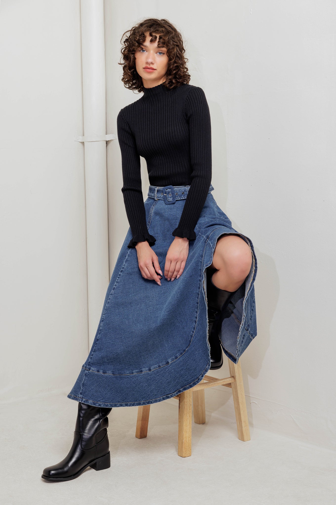 A washed denim midi skirt featuring circle skirt, self belt, uneven hemline and back zipper closure