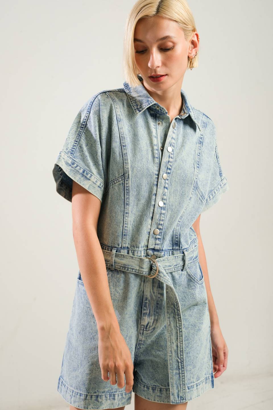 A washed denim romper featuring shirt collar, snap button down, short sleeve, self belt and side/back pockets
Details:
Self : 90% Cotton 10% Viscose
Size & Fit
- Model is 5`8" And Wearing Size Small
- Measurements Taken From Size Small
- Approx. Length: 32" Inseam: 3"