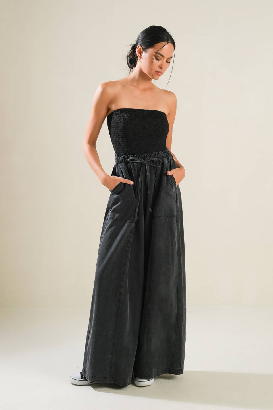 A mix media jumpsuit featuring strapless smocked tube top, contrasting pant with elasticized waist and tie, side pockets and wide leg