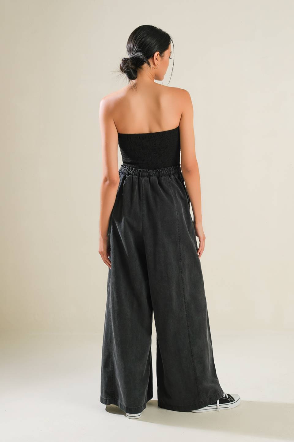 A mix media jumpsuit featuring strapless smocked tube top, contrasting pant with elasticized waist and tie, side pockets and wide leg