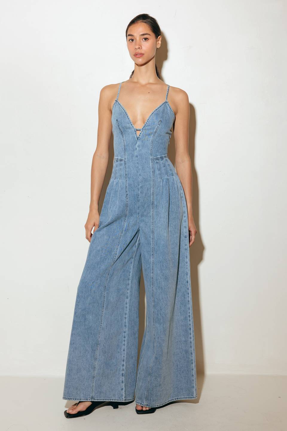A washed denim jumpsuit featuring cam top, front and back pintuck pleat, bare back with strap and zipper closure.