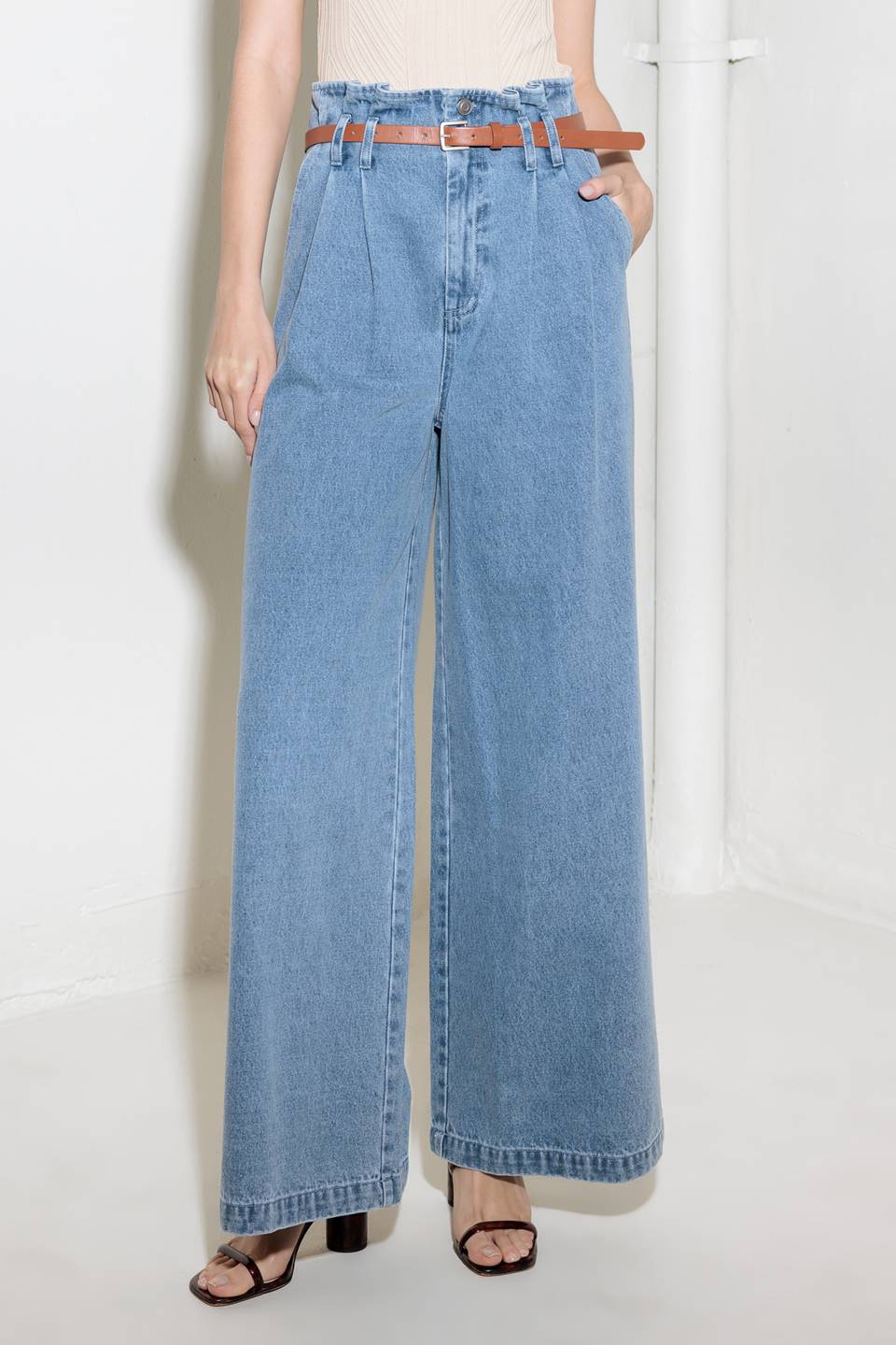 A washed denim pant featuring paper bag waist, belt, front closure, side pocket and wide leg closure.