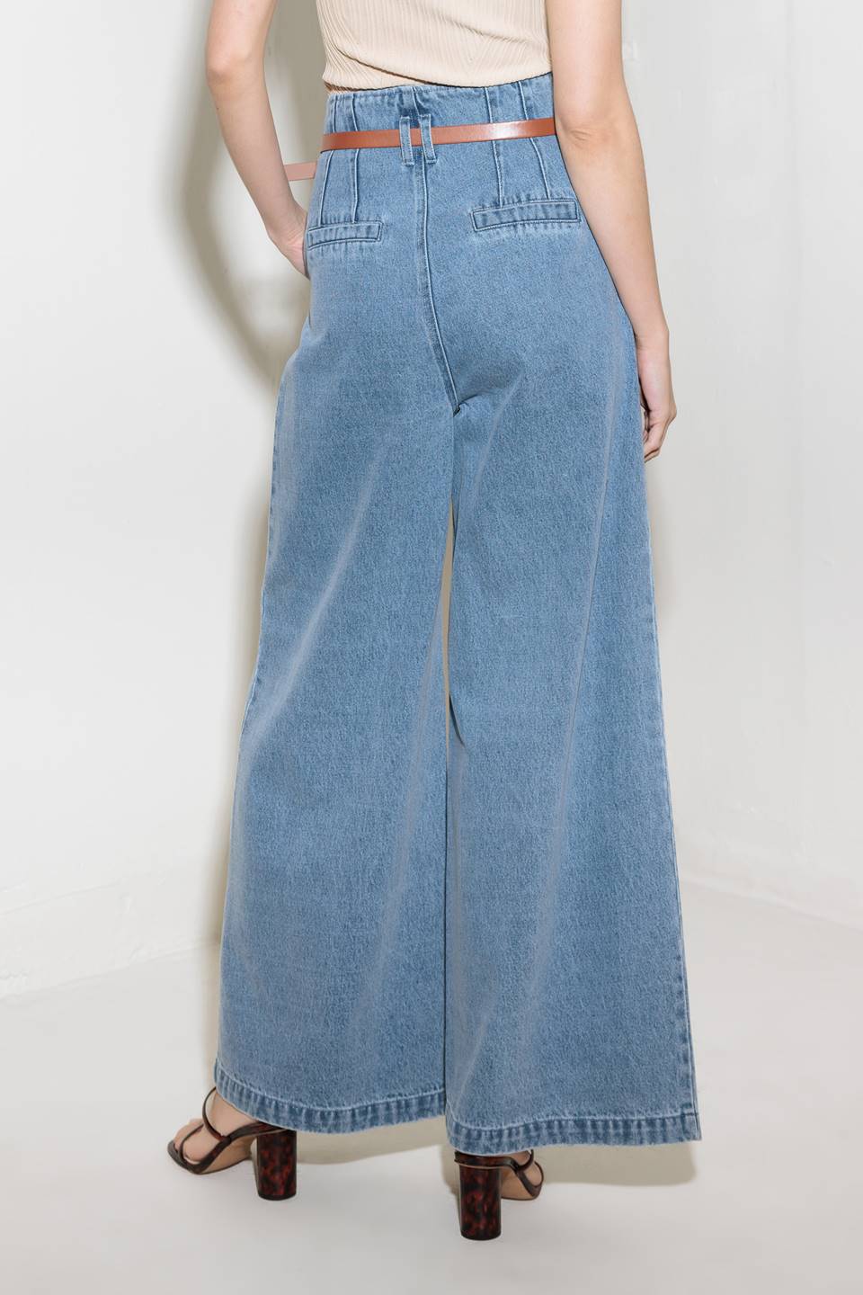 A washed denim pant featuring paper bag waist, belt, front closure, side pocket and wide leg closure.
