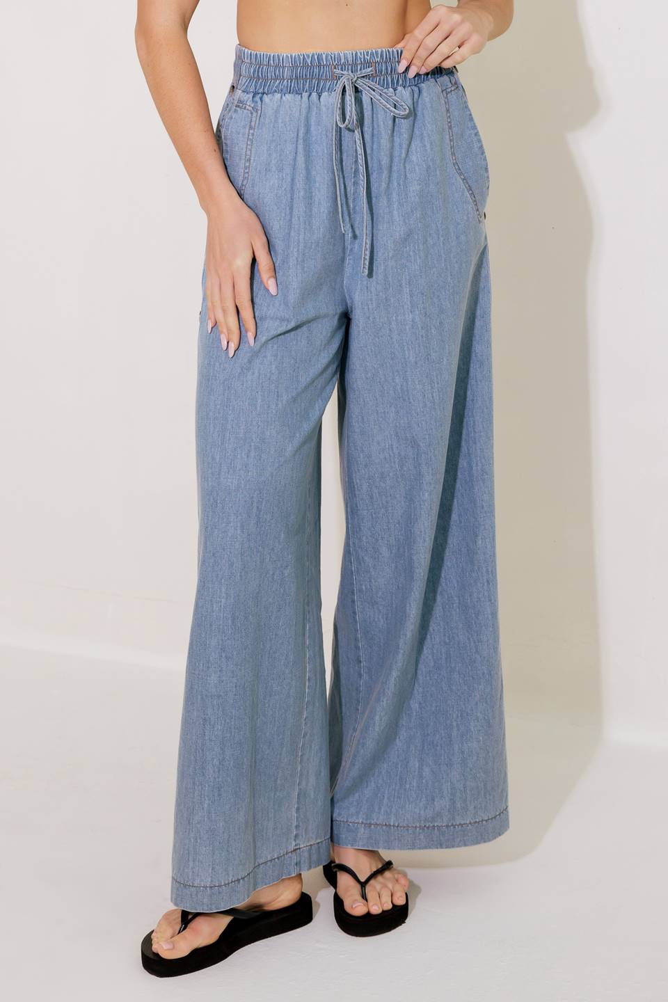 A chambray pant featuring elasticized waist with tie, side pockets, side button down and wide leg