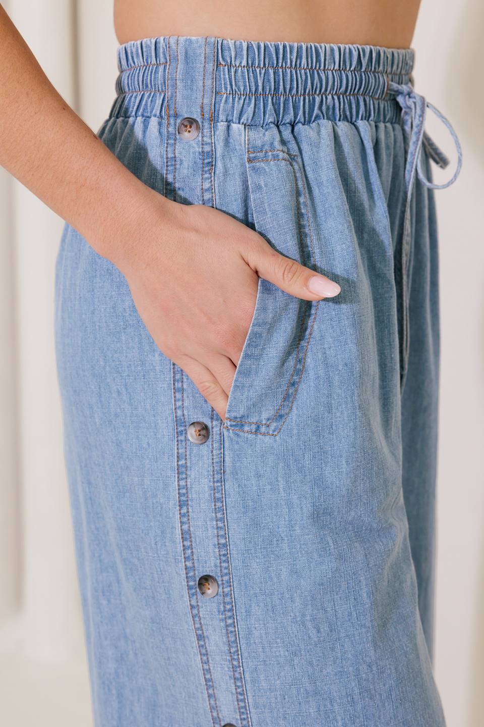 A chambray pant featuring elasticized waist with tie, side pockets, side button down and wide leg