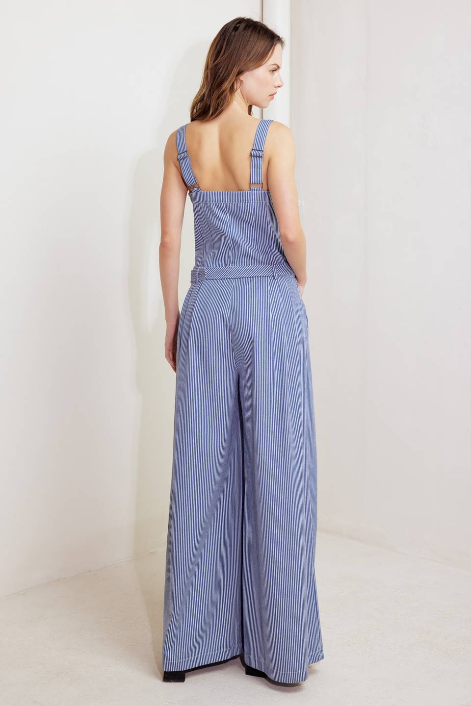 A striped woven jumpsuit featuring straight neckline, straps, front closure, self belt, side pockets and wide leg.