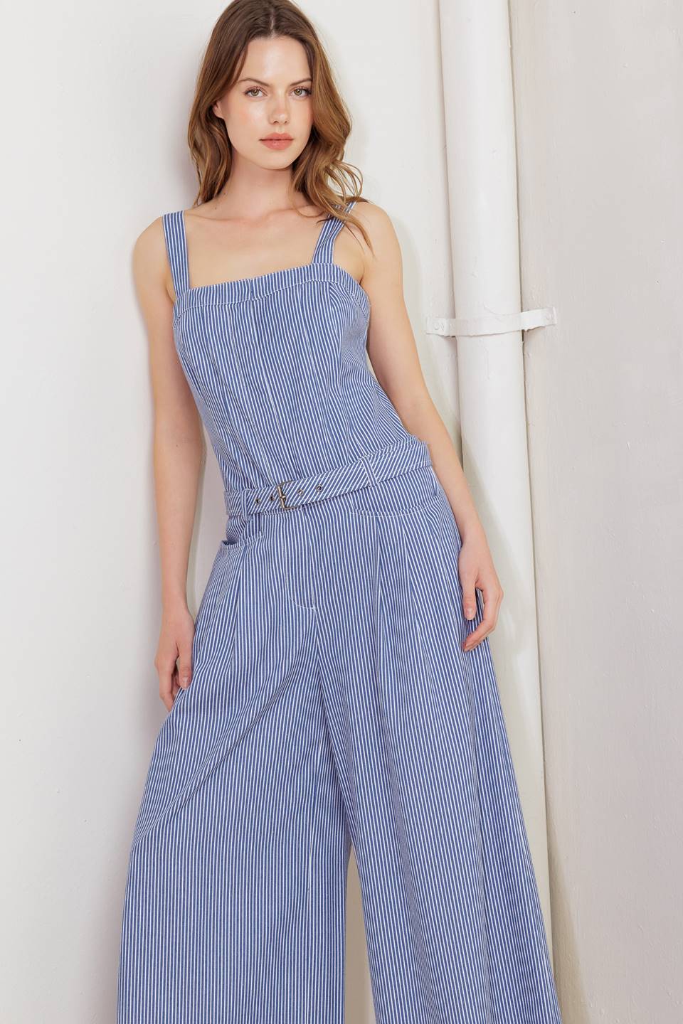 A striped woven jumpsuit featuring straight neckline, straps, front closure, self belt, side pockets and wide leg.