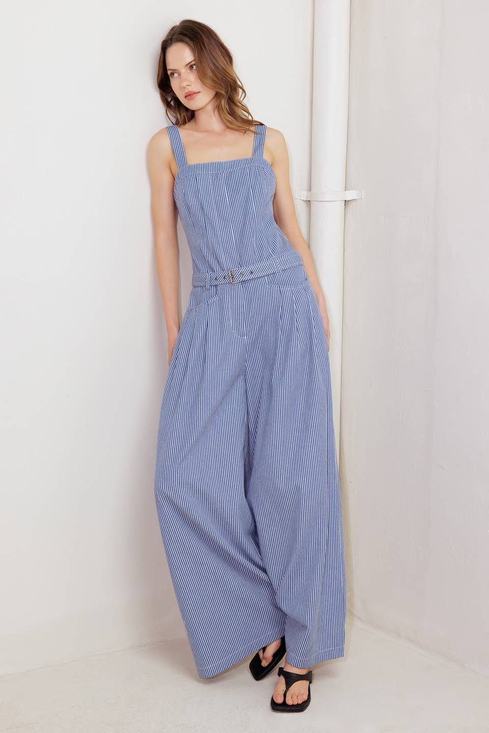 A striped woven jumpsuit featuring straight neckline, straps, front closure, self belt, side pockets and wide leg.