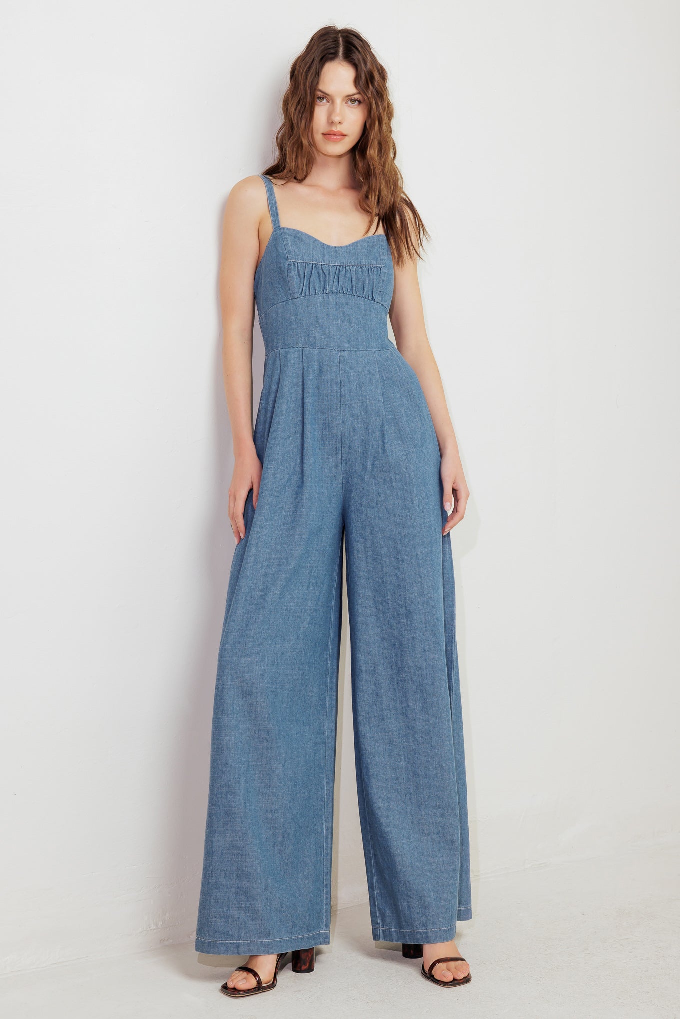 A washed lightweight denim jumpsuit featuring sweetheart neckline, straps, waist yoke, wide leg, bare back with zipper closure