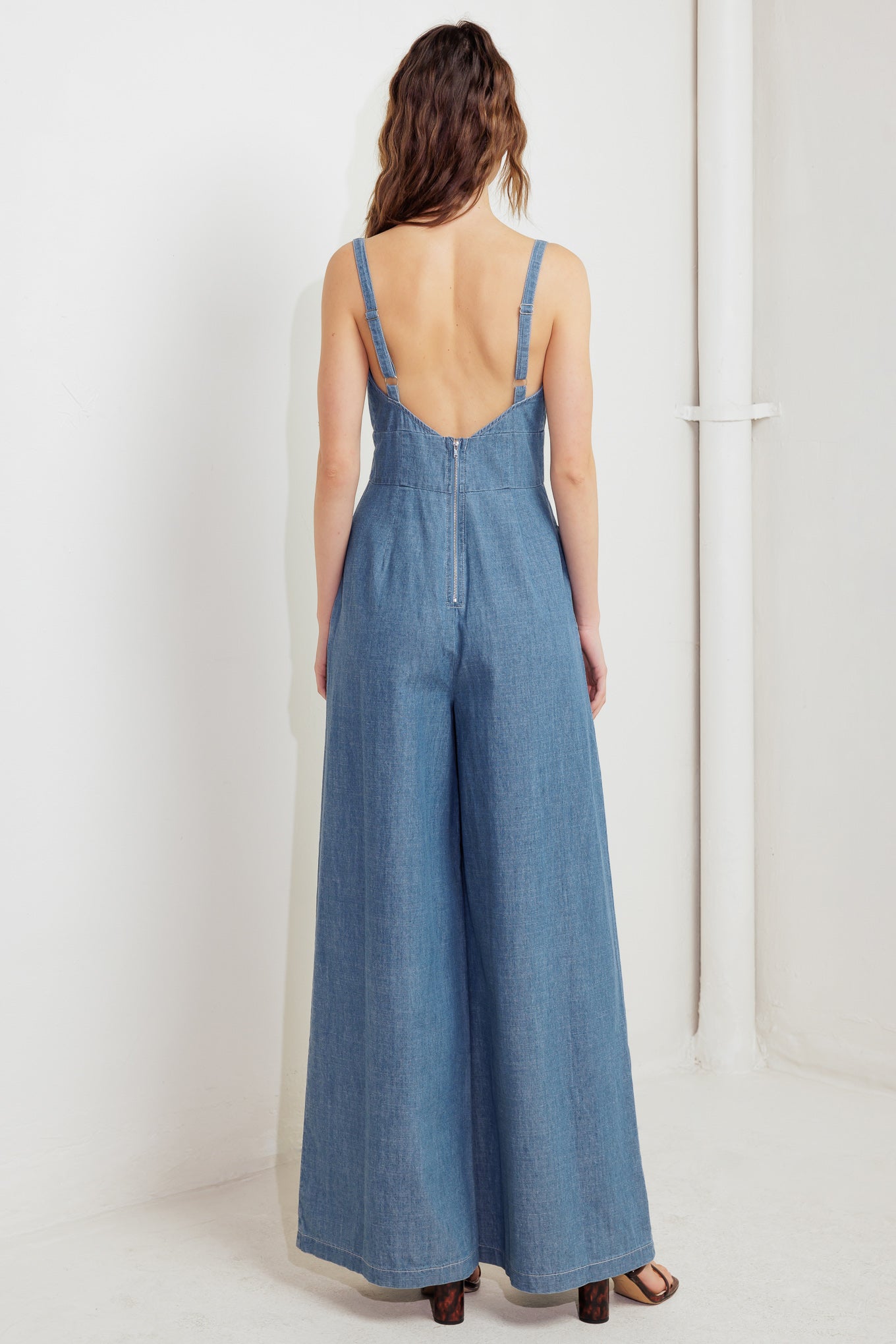 A washed lightweight denim jumpsuit featuring sweetheart neckline, straps, waist yoke, wide leg, bare back with zipper closure