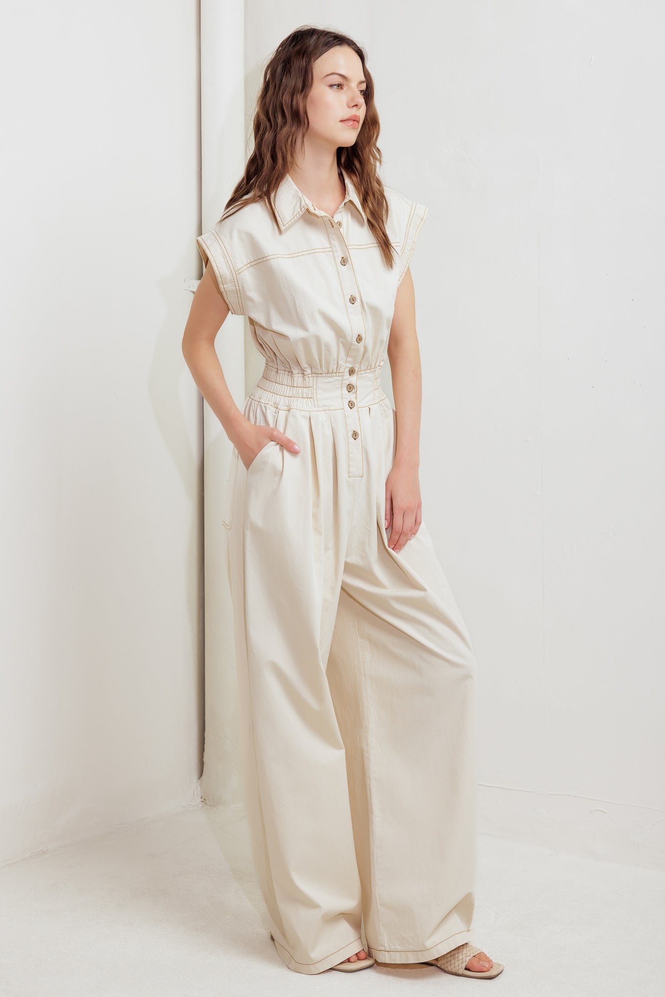 A solid woven jumpsuit featuring collar, dropped shoulder with short sleeve, button down, elasticized waistband, side pockets and wide leg