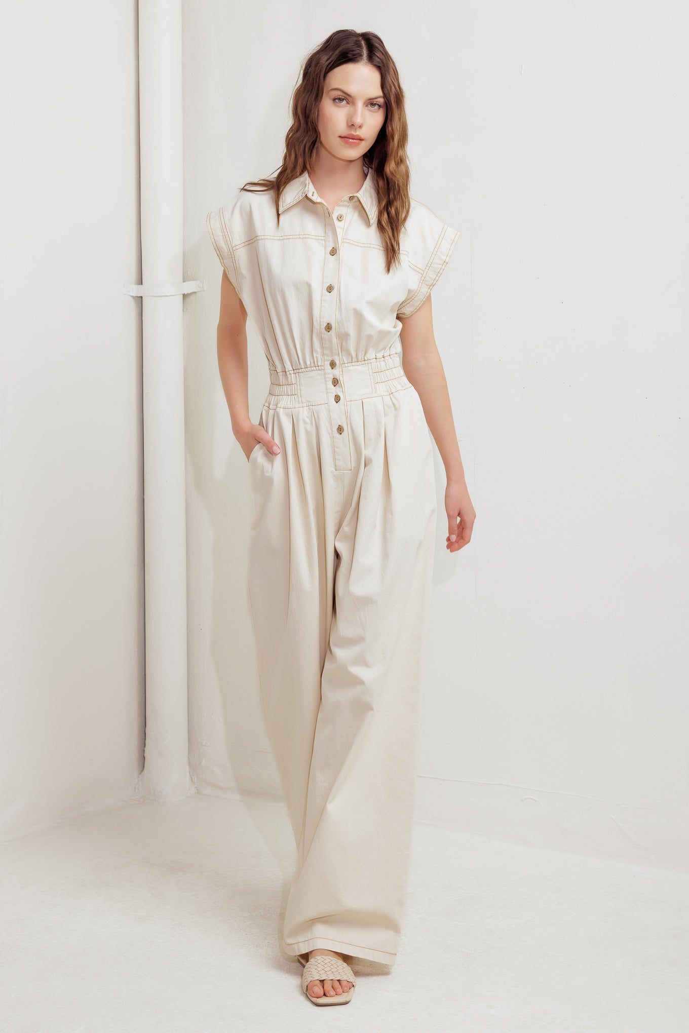 A solid woven jumpsuit featuring collar, dropped shoulder with short sleeve, button down, elasticized waistband, side pockets and wide leg