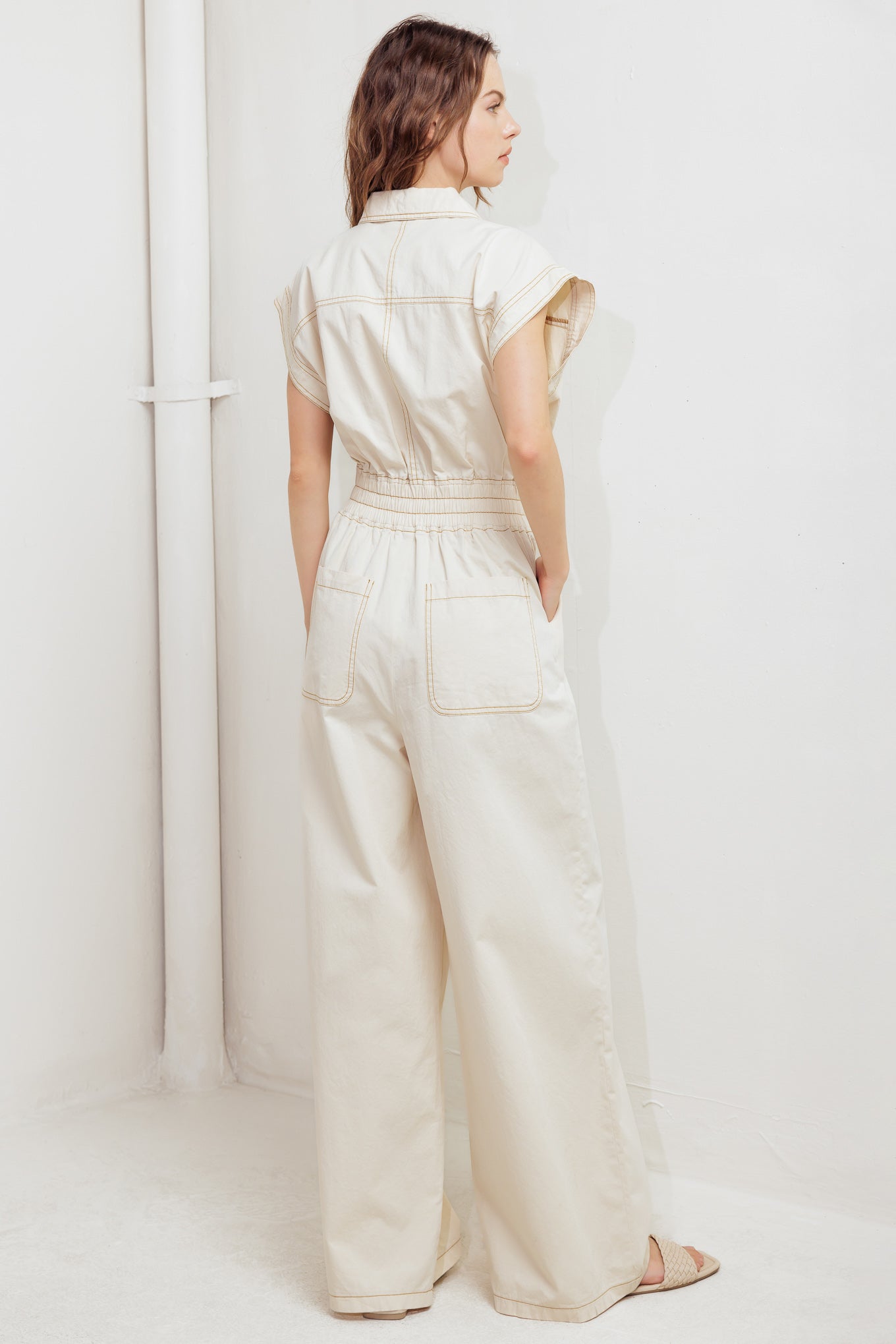 A solid woven jumpsuit featuring collar, dropped shoulder with short sleeve, button down, elasticized waistband, side pockets and wide leg