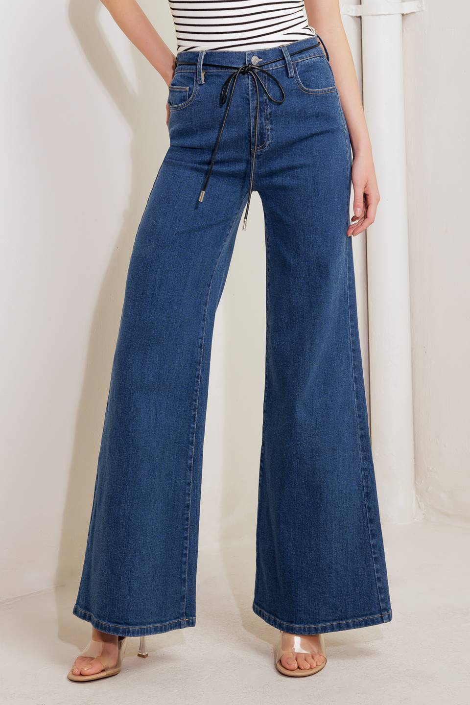 A washed denim pant featuring front closure, contrasting skinny belt and boot leg.
