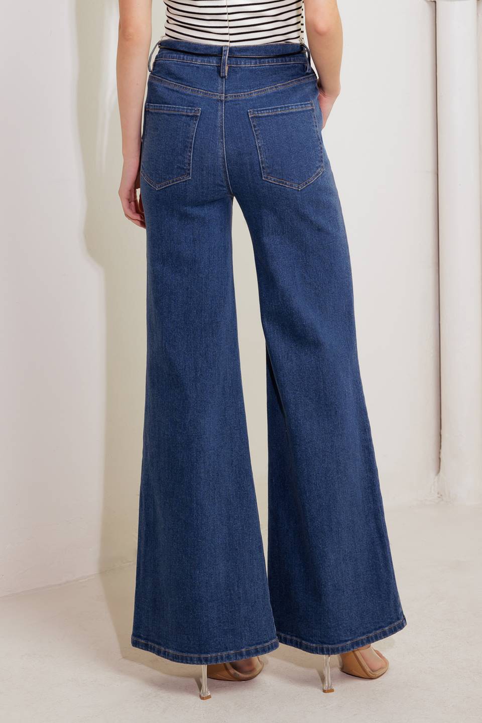 A washed denim pant featuring front closure, contrasting skinny belt and boot leg.