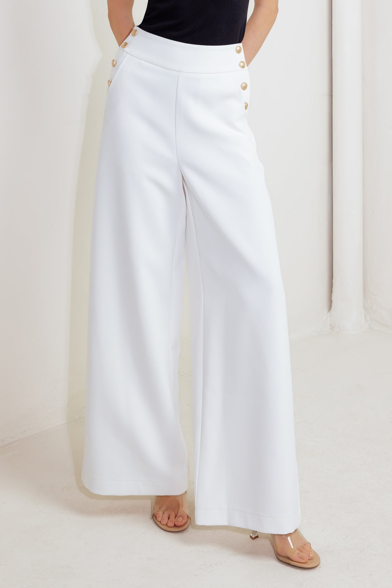 White wide-leg pants with gold buttons worn by a person on a white background