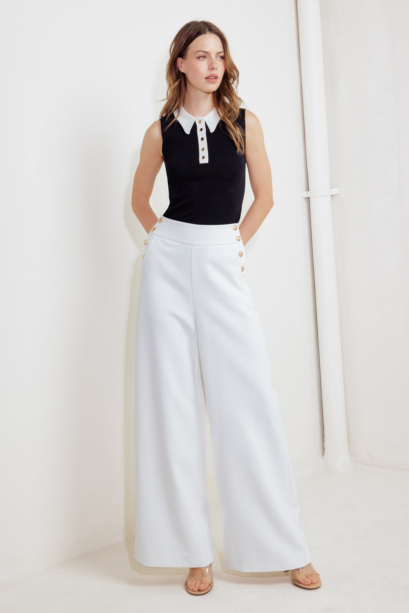 A solid white woven pant featuring side button detail, pockets, wide leg and back zipper