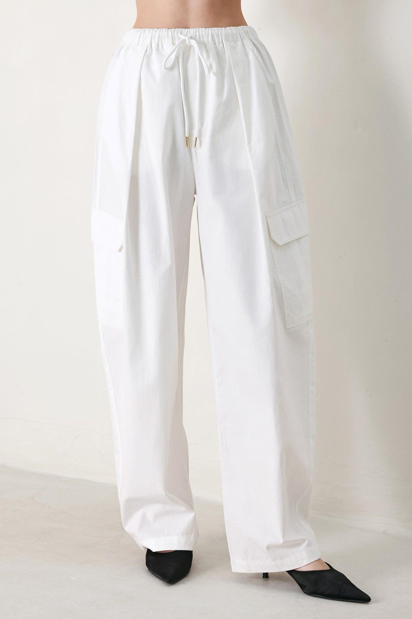 A solid woven balloon pant featuring elastic waist with tie and pockets
