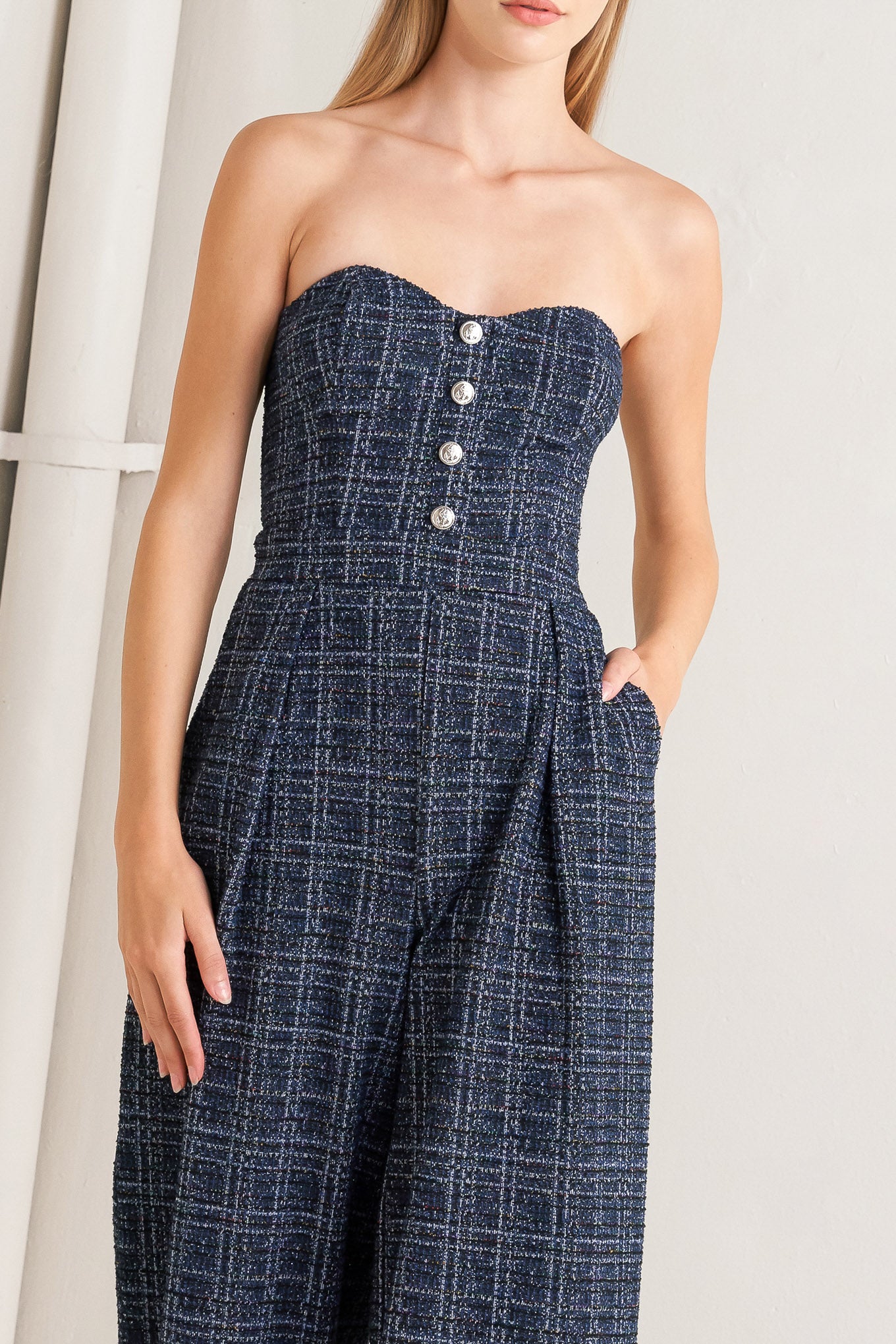 A tweed jumpsuit featuring sweetheart neckline, front button detail, side pockets and back zipper closure