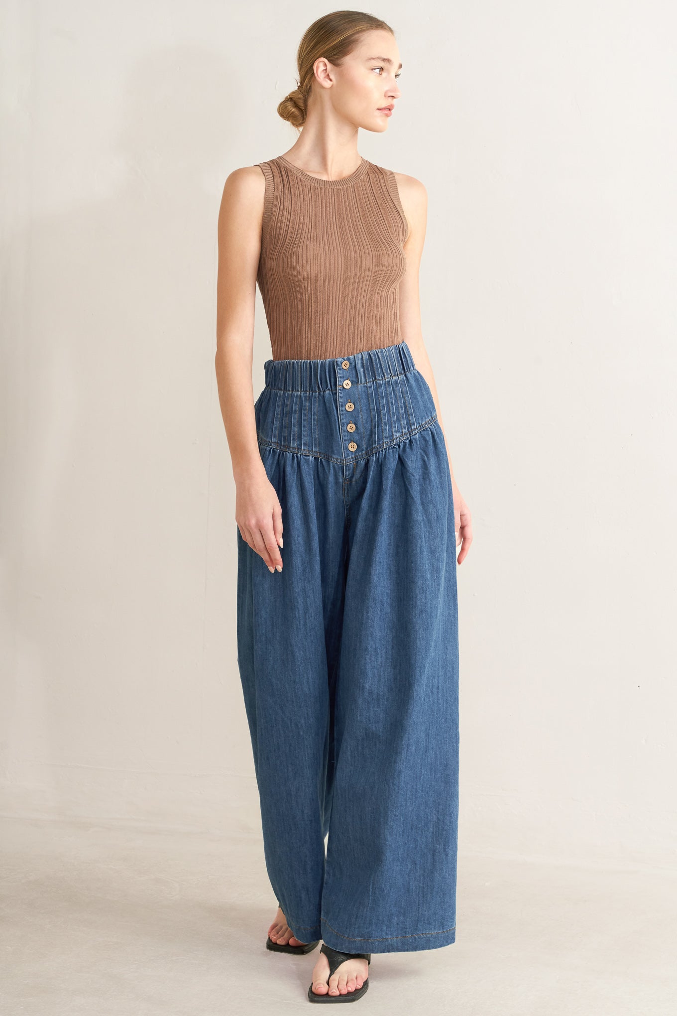 Woman wearing a brown sleeveless top and blue wide-leg pants on a beige background