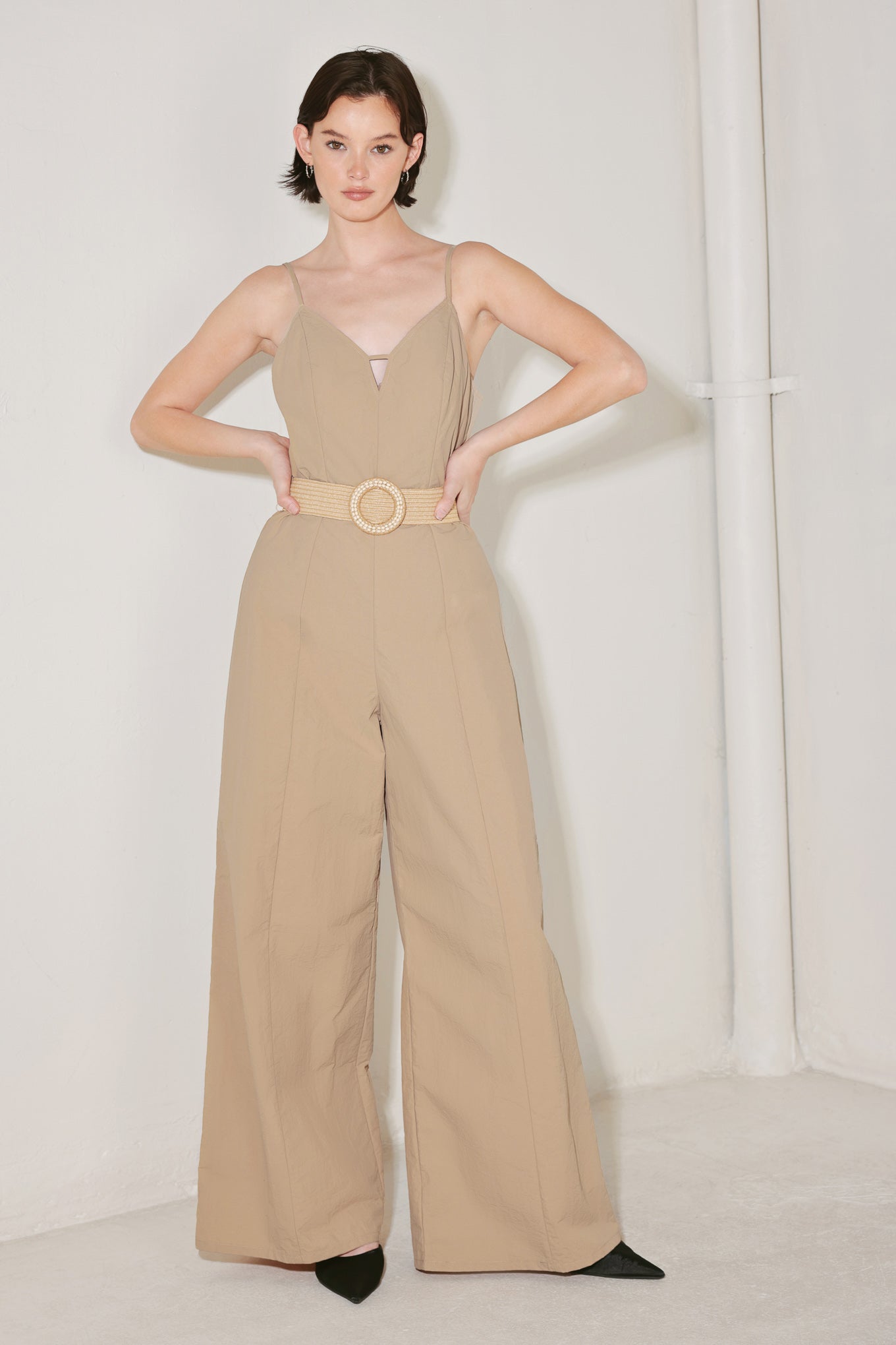 Woman wearing a beige jumpsuit featuring cami top, straps, contrasting belt, wide leg and back zipper closure | FREEMARKET | Flying Tomato