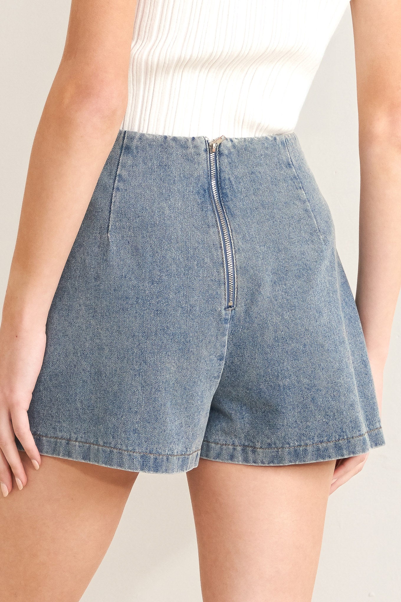 Denim shorts worn by a person on a plain background