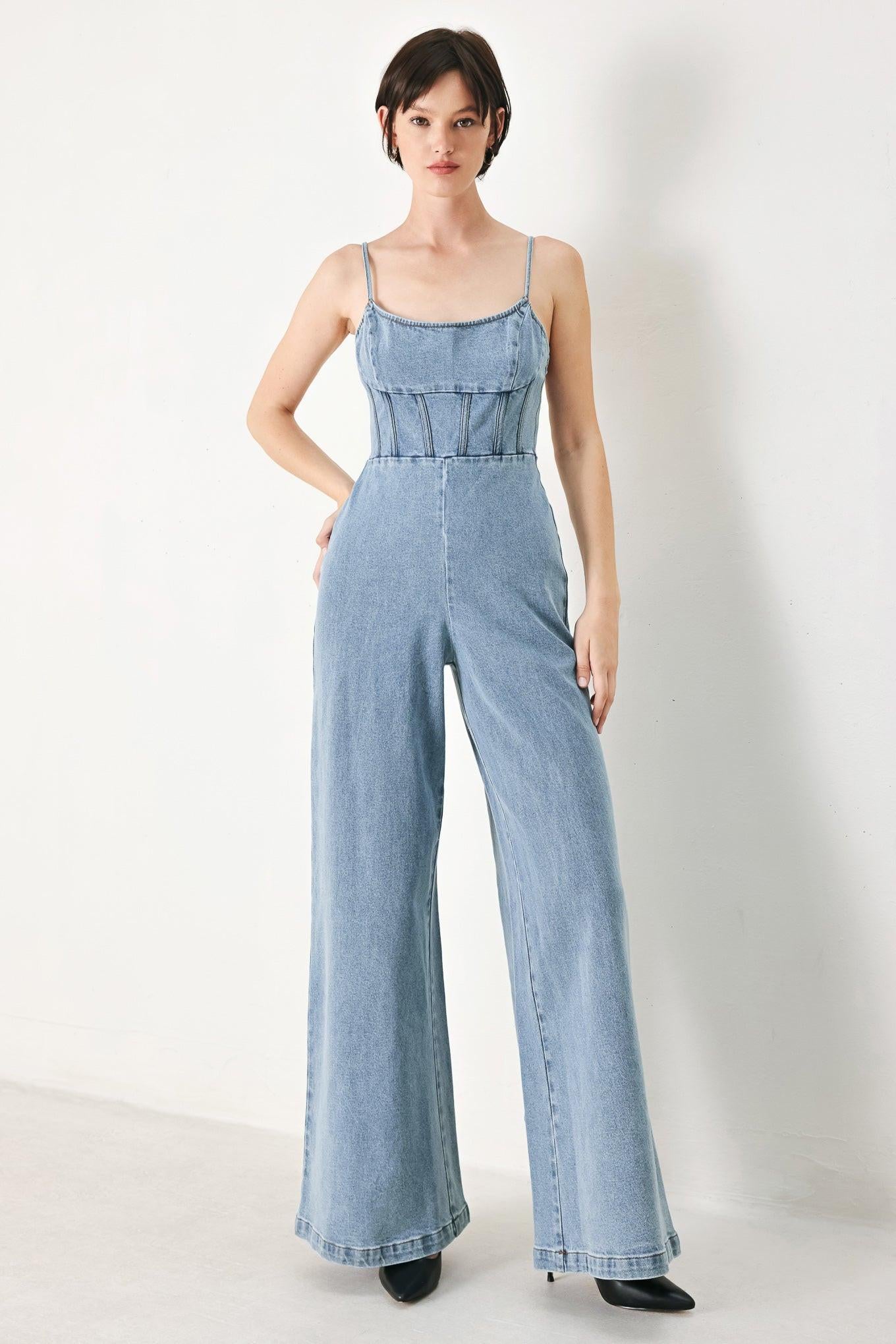 A washed denim jumpsuit featuring U neckline, straps, waist yoke, wide leg, bare back with zipper closure