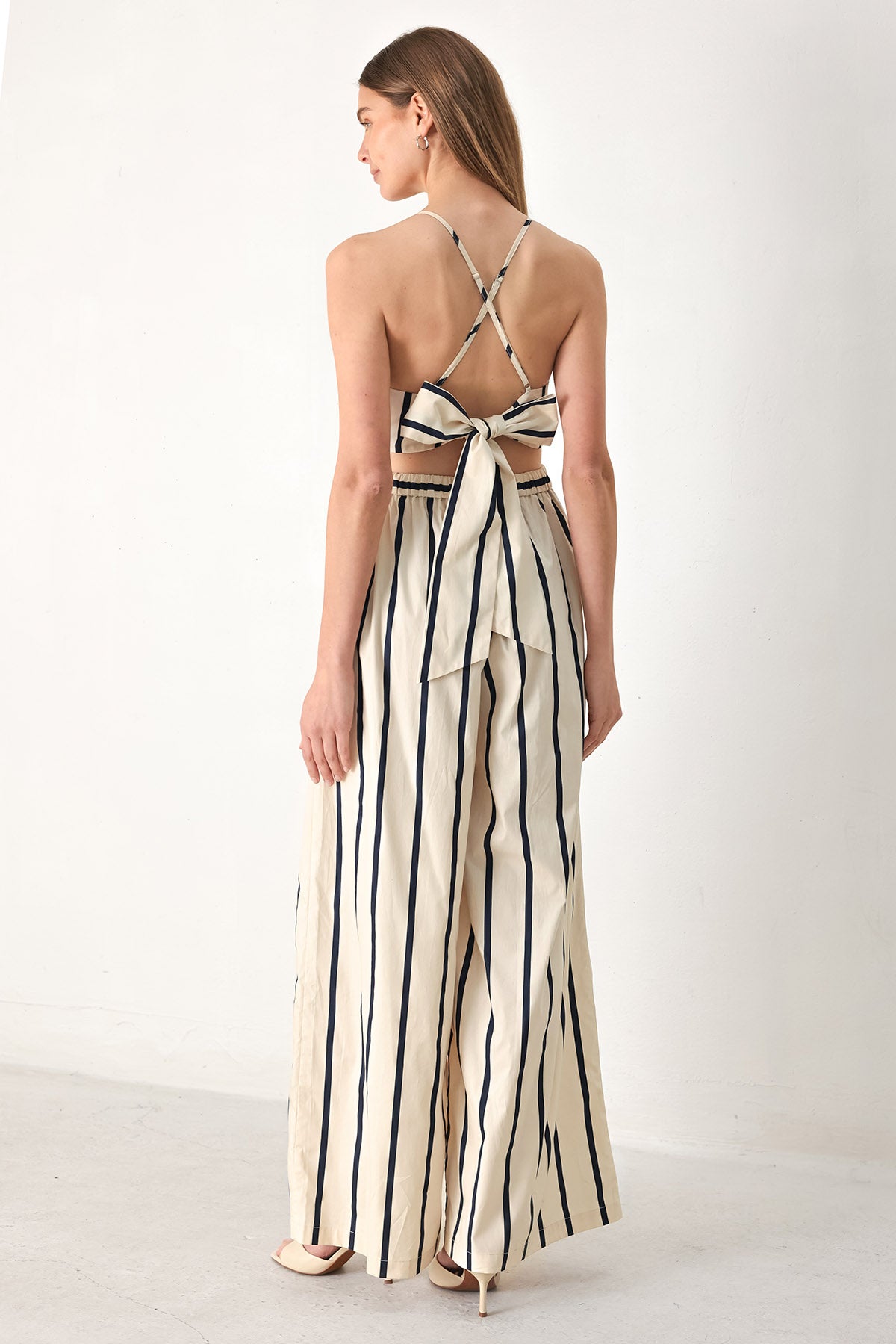 Woman wearing a navy and ivory striped jumpsuit featuring straight neckline, side pockets, bare back with tie and wide leg | FREEMARKET | Flying Tomato