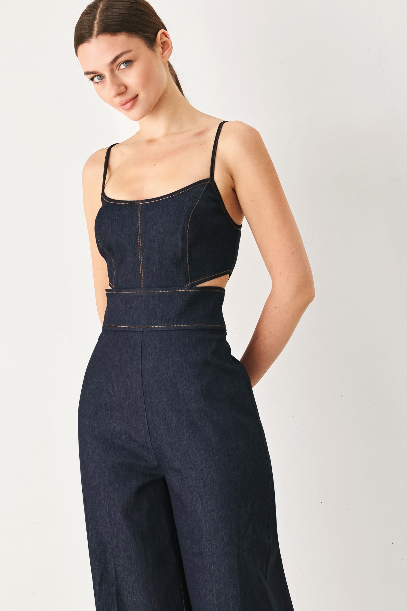 Woman wearing a dark denim jumpsuit jumpsuit featuring U neckline, straps, side cut out, wide leg and back zipper closure | FREEMARKET