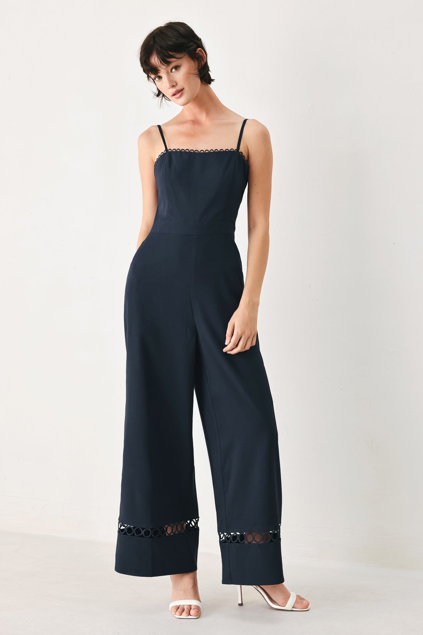 Woman wearing a navy wide leg jumpsuit straight neckline with trim edge, straps, with lace inset and back zipper closure | FREEMARKET